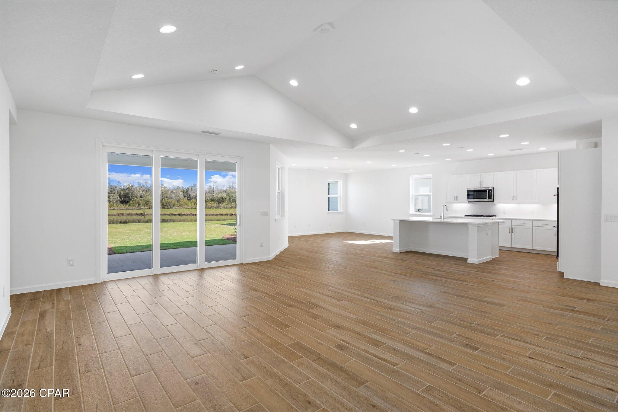 Open-plan living area with wood-look tile floors, vaulted ceiling, kitchen island, and sliding doors overlooking a pond.