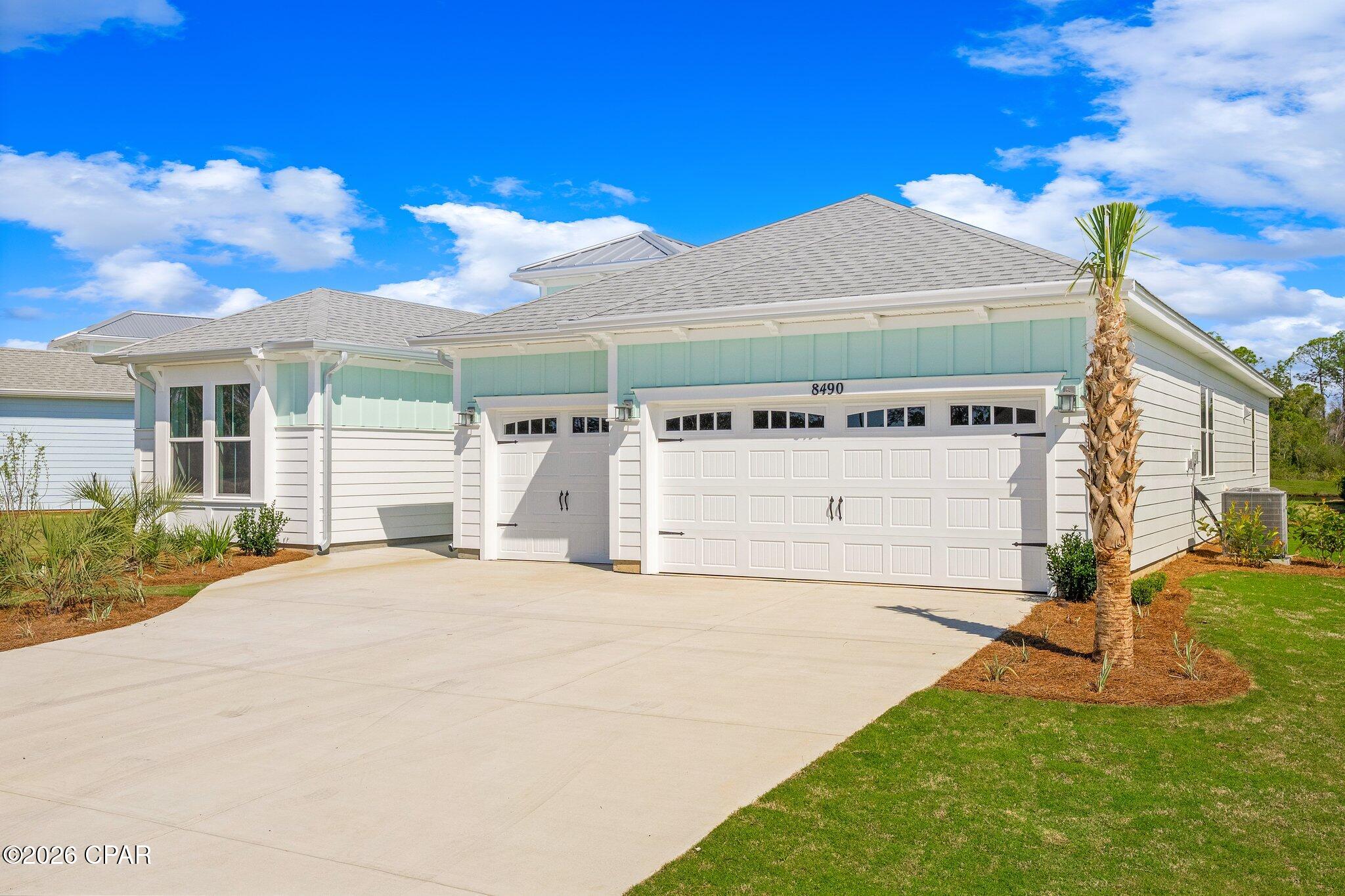 Home exterior with two garage doors, a wide driveway, and a palm tree beside the lawn.