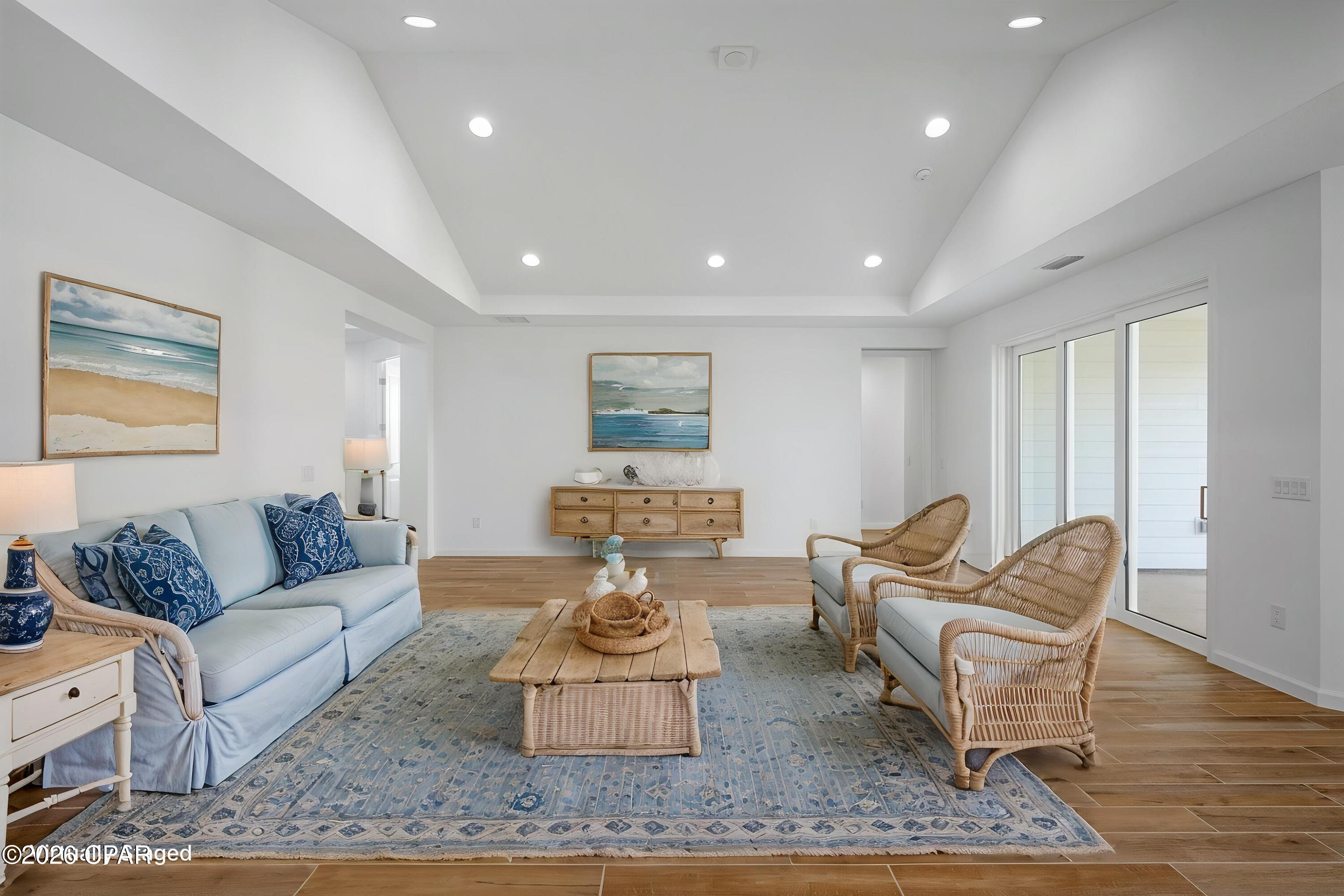 Living room with a pale blue sofa, wicker armchairs, a blue patterned rug, and sliding glass doors.