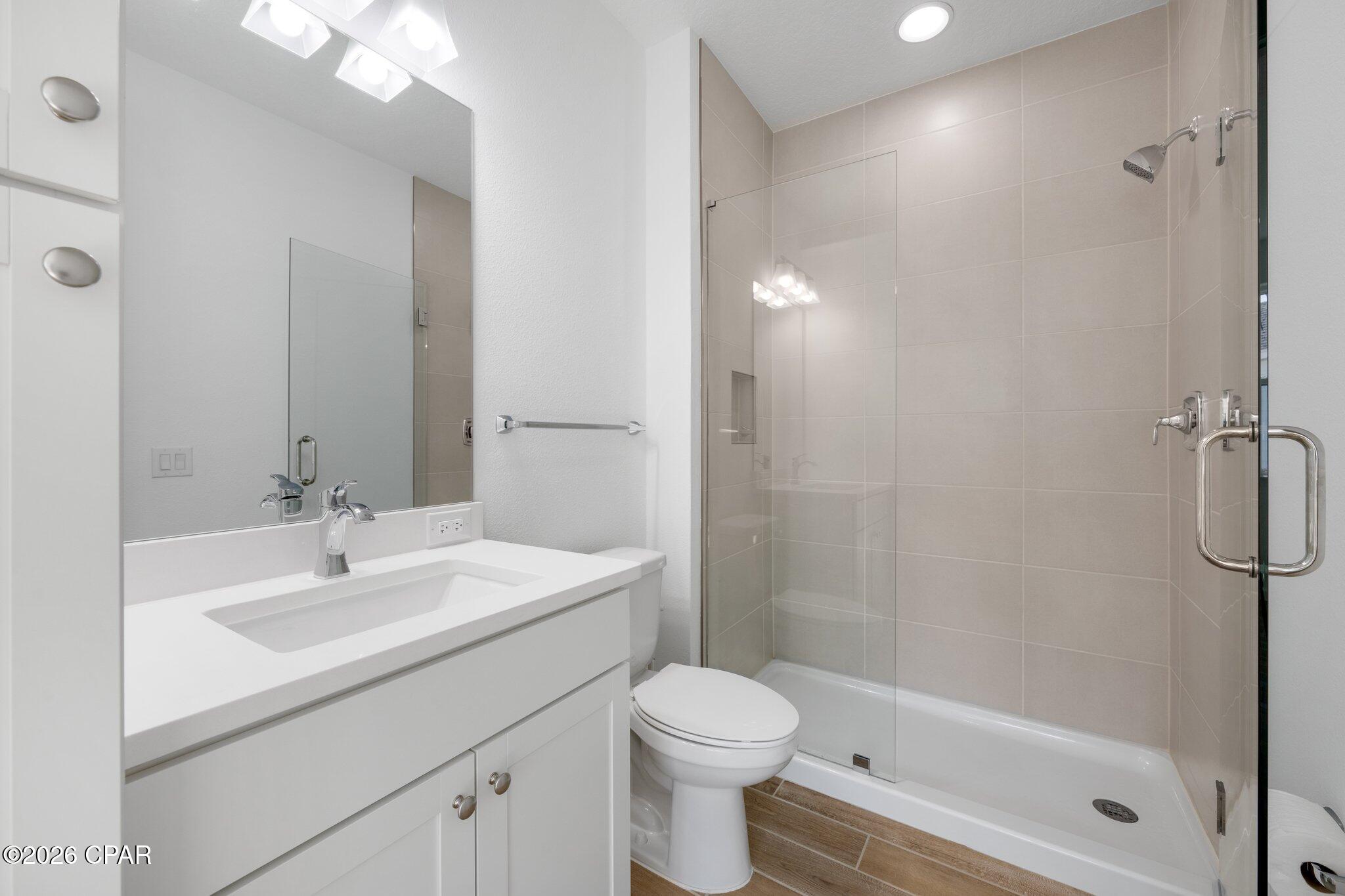 Bathroom with a white vanity and sink beside a glass-enclosed tub-shower with beige tile.