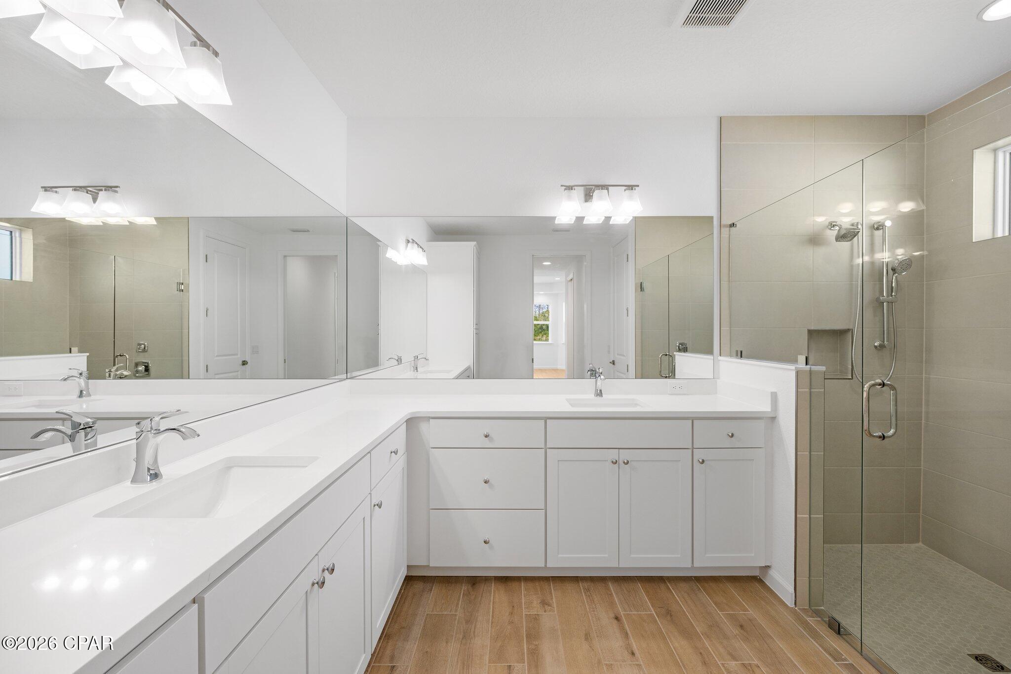 Bathroom with a long white vanity, large mirrors, and a glass-enclosed tiled shower.