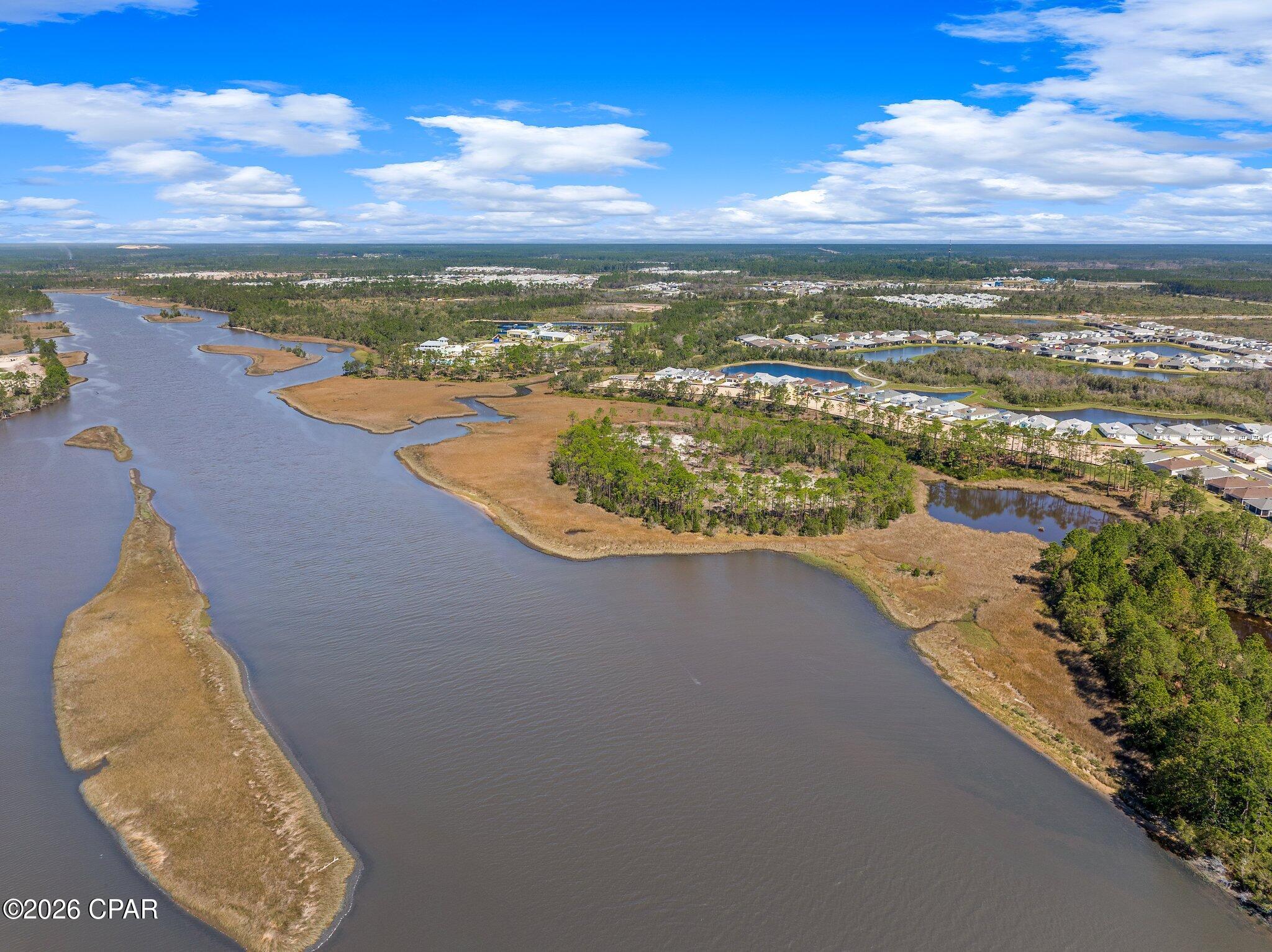 Aerial view of a winding waterway, marshland, wooded shoreline, and nearby homes.
