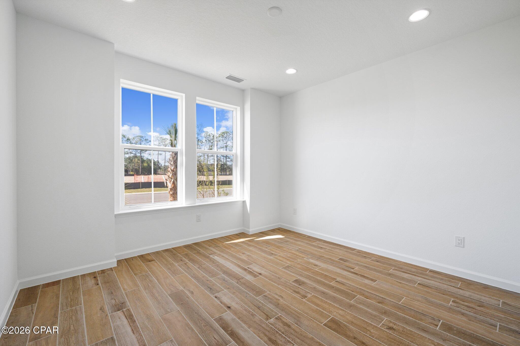 Vacant room with wood-look tile flooring and two bright windows.