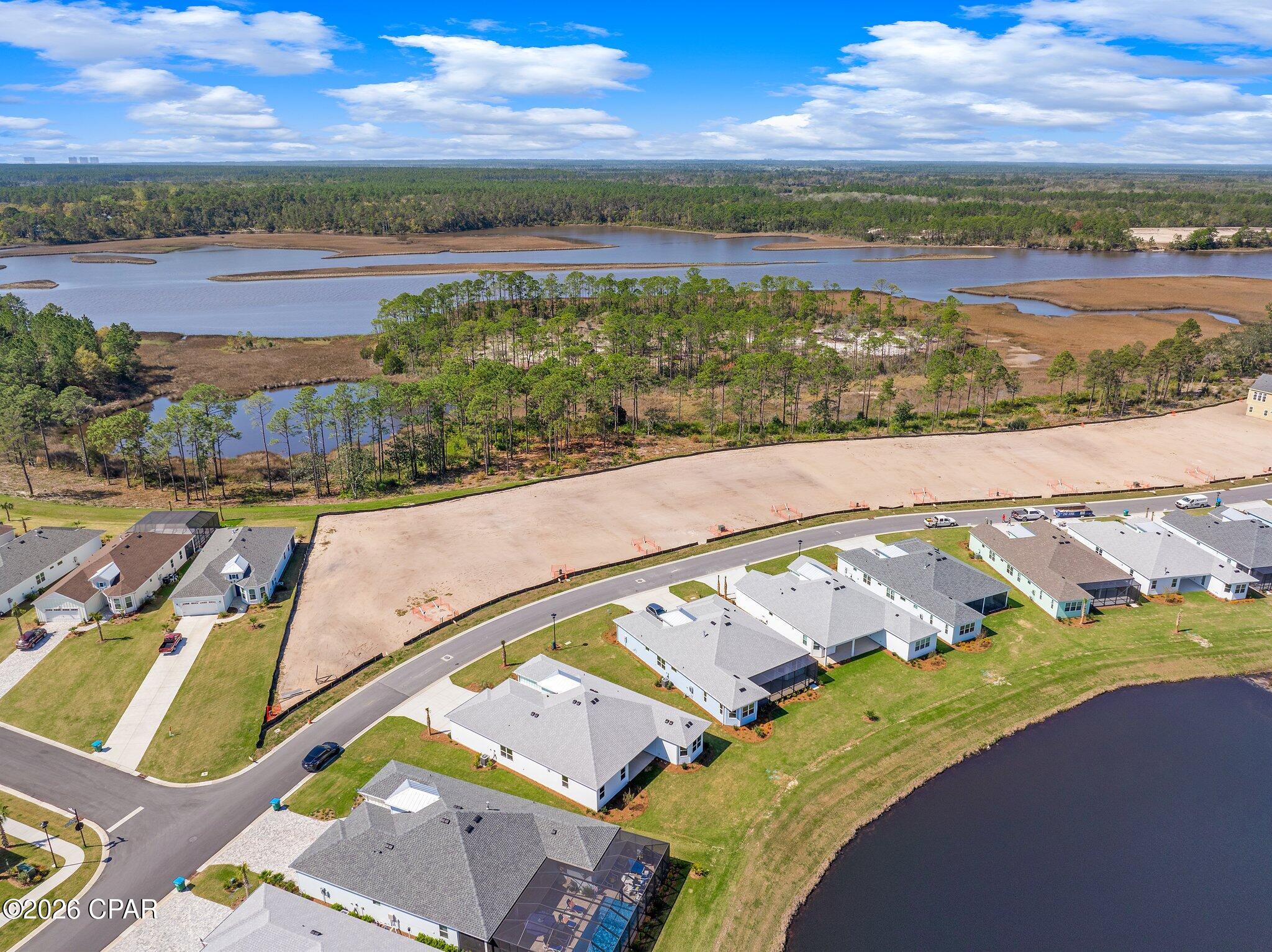 Aerial view of a graded subdivision lot beside marshland and water, surrounded by homes.