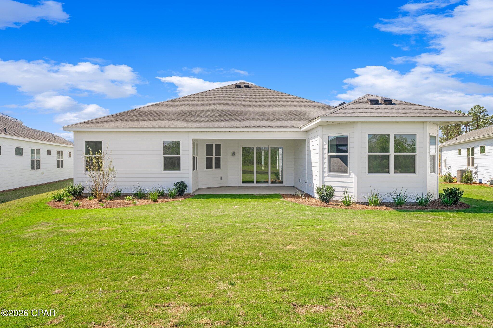 Rear of a white home with a covered patio, sliding doors, and a broad green lawn.