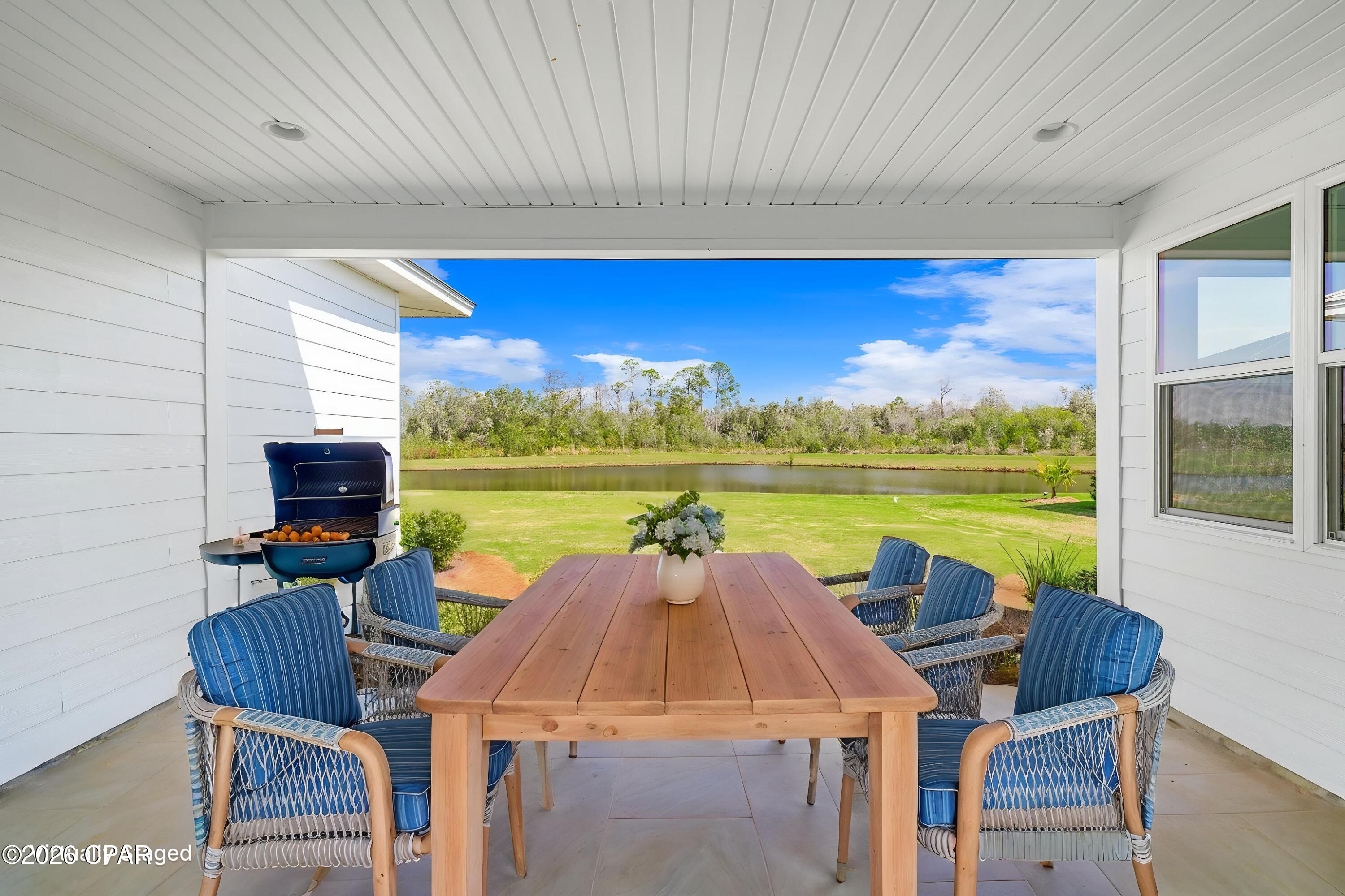 Covered patio dining area with blue chairs and a wooden table overlooking a pond.