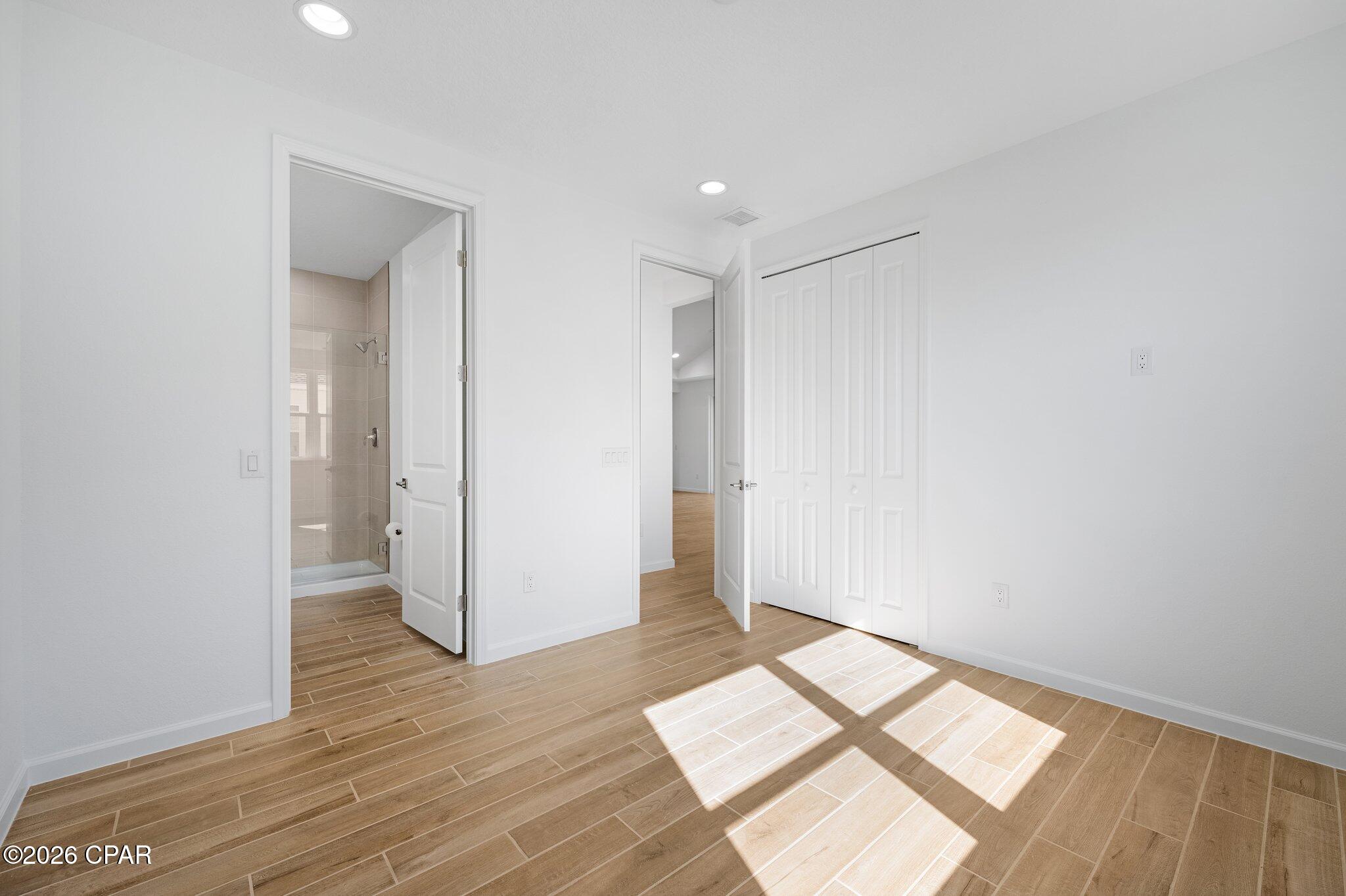 Empty bedroom with wood-look tile flooring, double closet, and adjoining tiled shower.