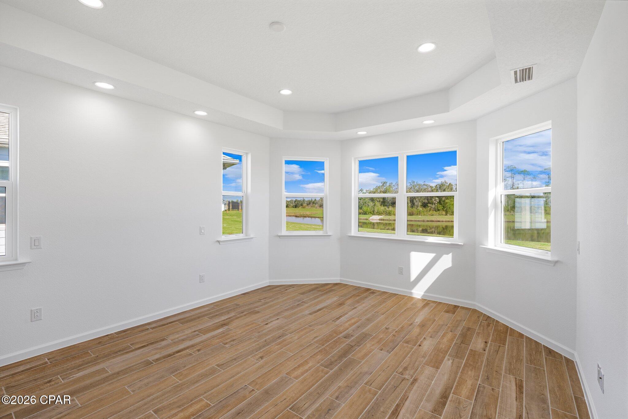 Empty bright room with wood-look tile floors and large windows overlooking a pond.