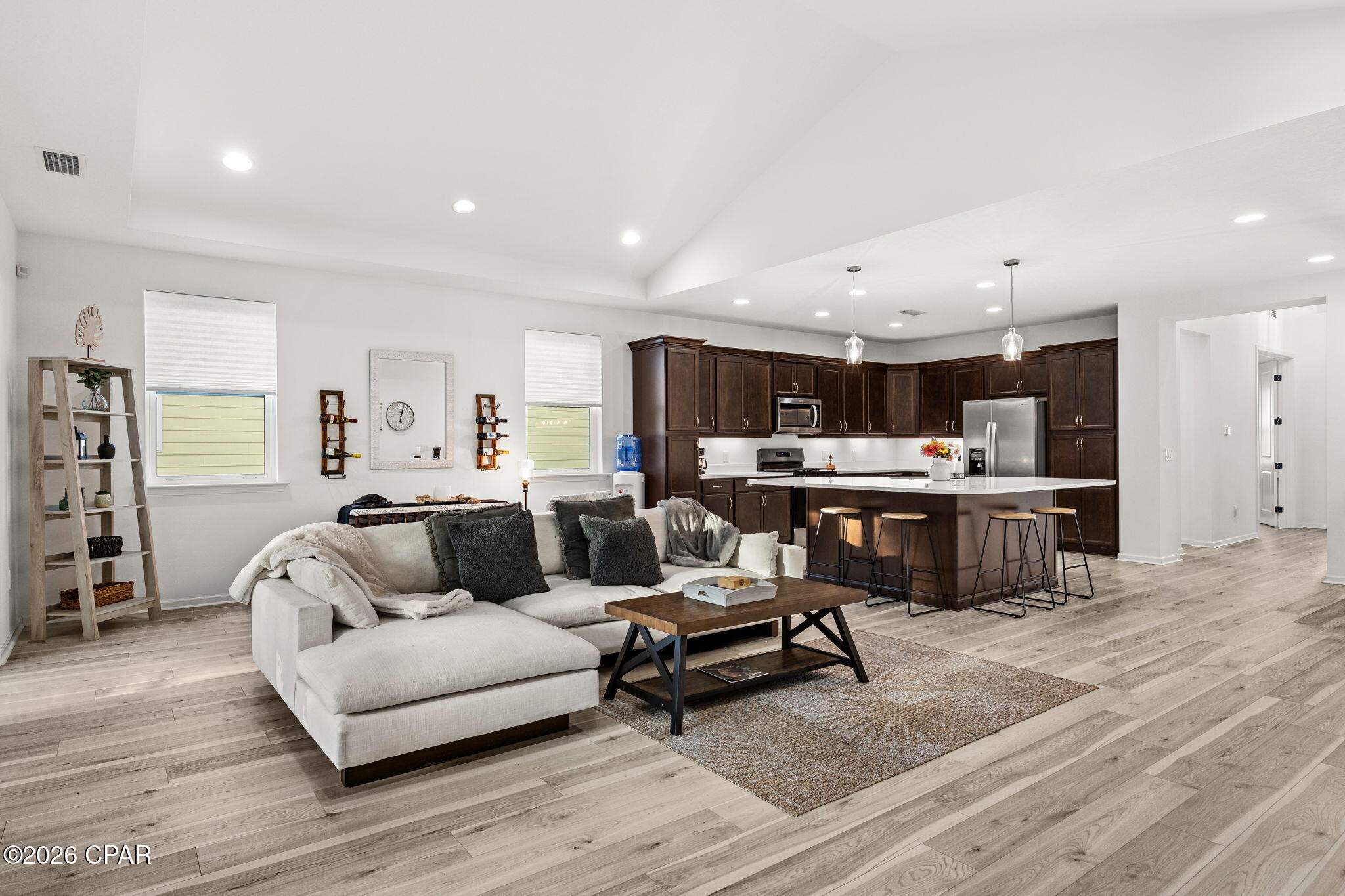 Open-plan living room and kitchen with a light sectional, dark wood cabinets, and a bar island.