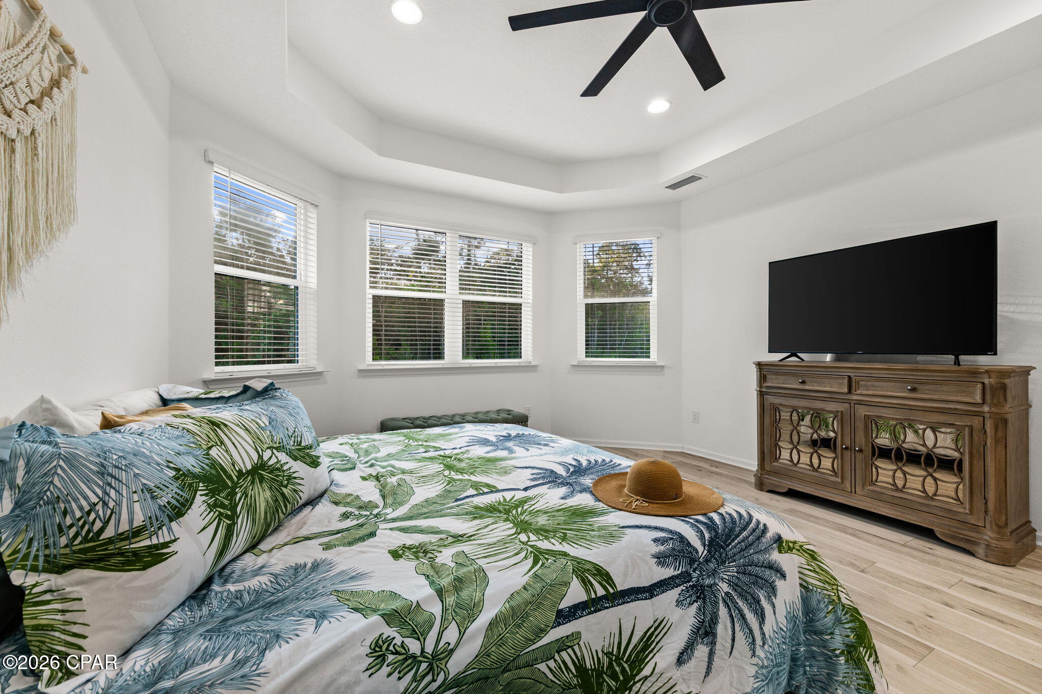 Bedroom with tropical leaf-print bedding, multiple windows, and a TV on a wooden console.