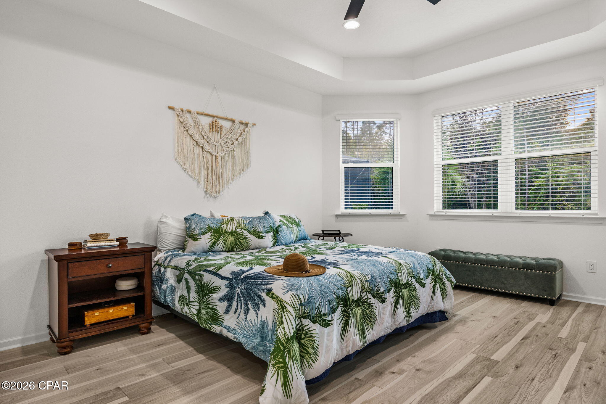 Bedroom with tropical-leaf bedding, a straw hat on the bed, and a green upholstered bench.