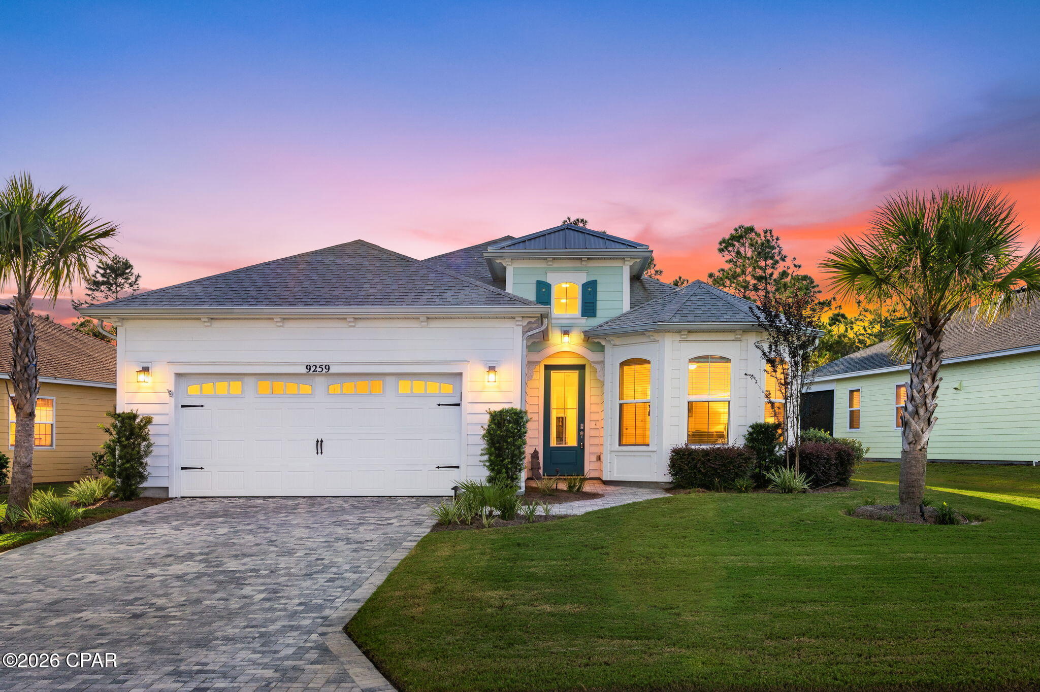 White house with a double garage and teal entry, illuminated against a colorful dusk sky.
