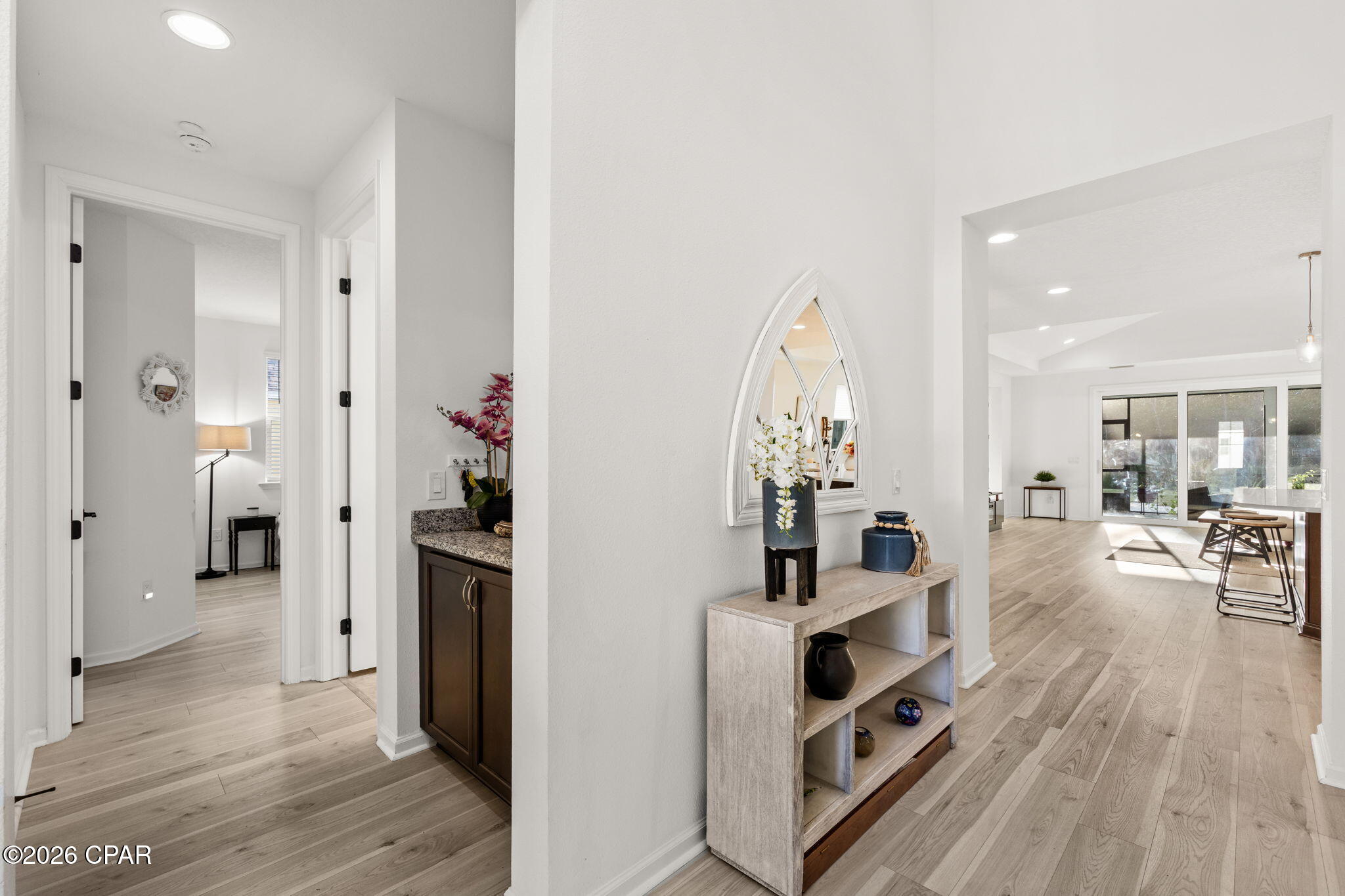Bright entry hall with pale wood floors, an arched mirror, console table, and sunlit living area.