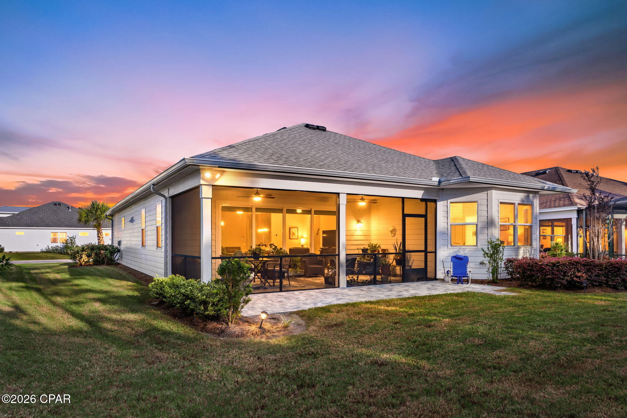 Rear of a single-story home with a spacious screened porch glowing at sunset.