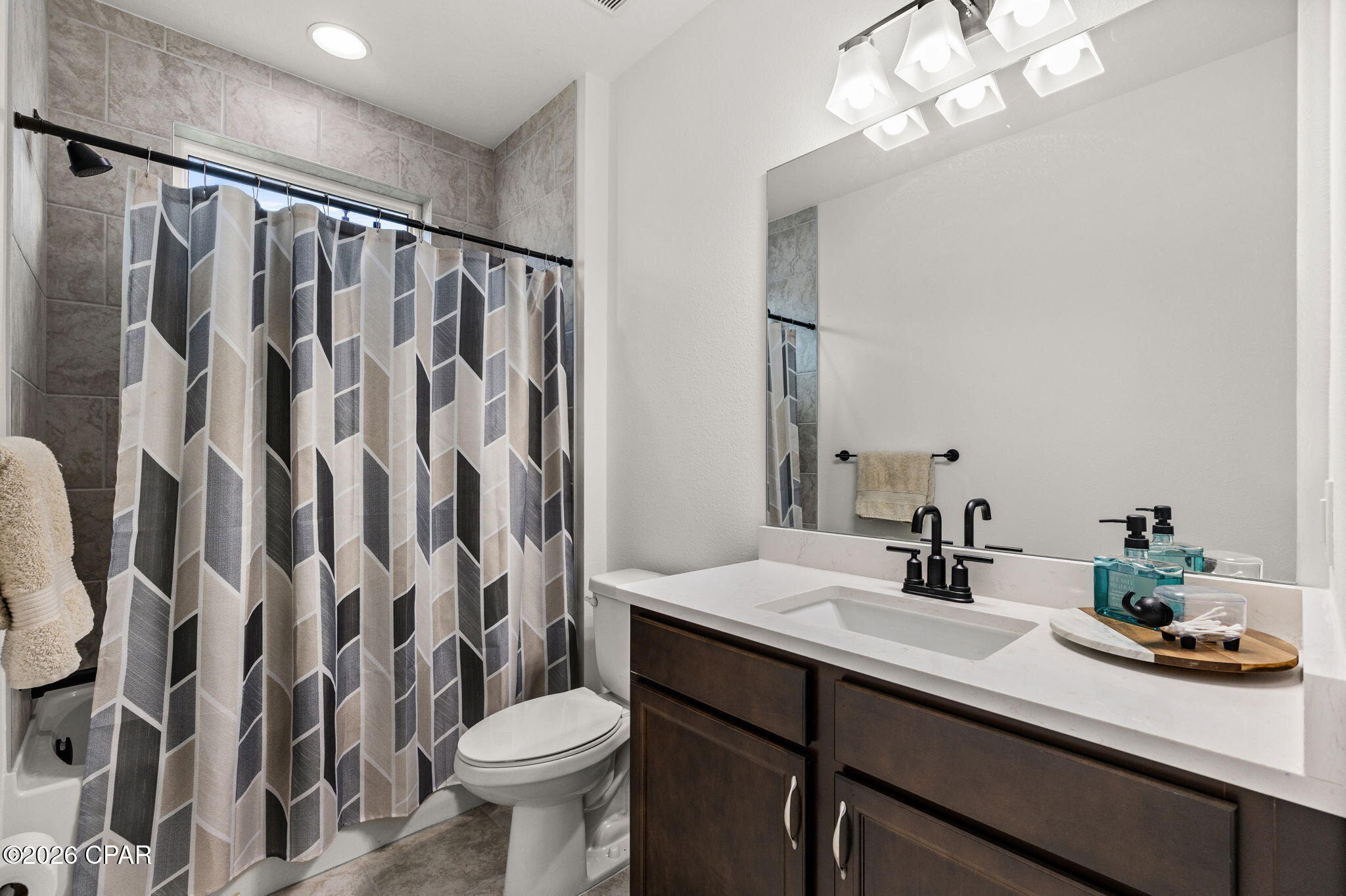 Bathroom with geometric shower curtain, dark wood vanity, white countertop, and black fixtures.