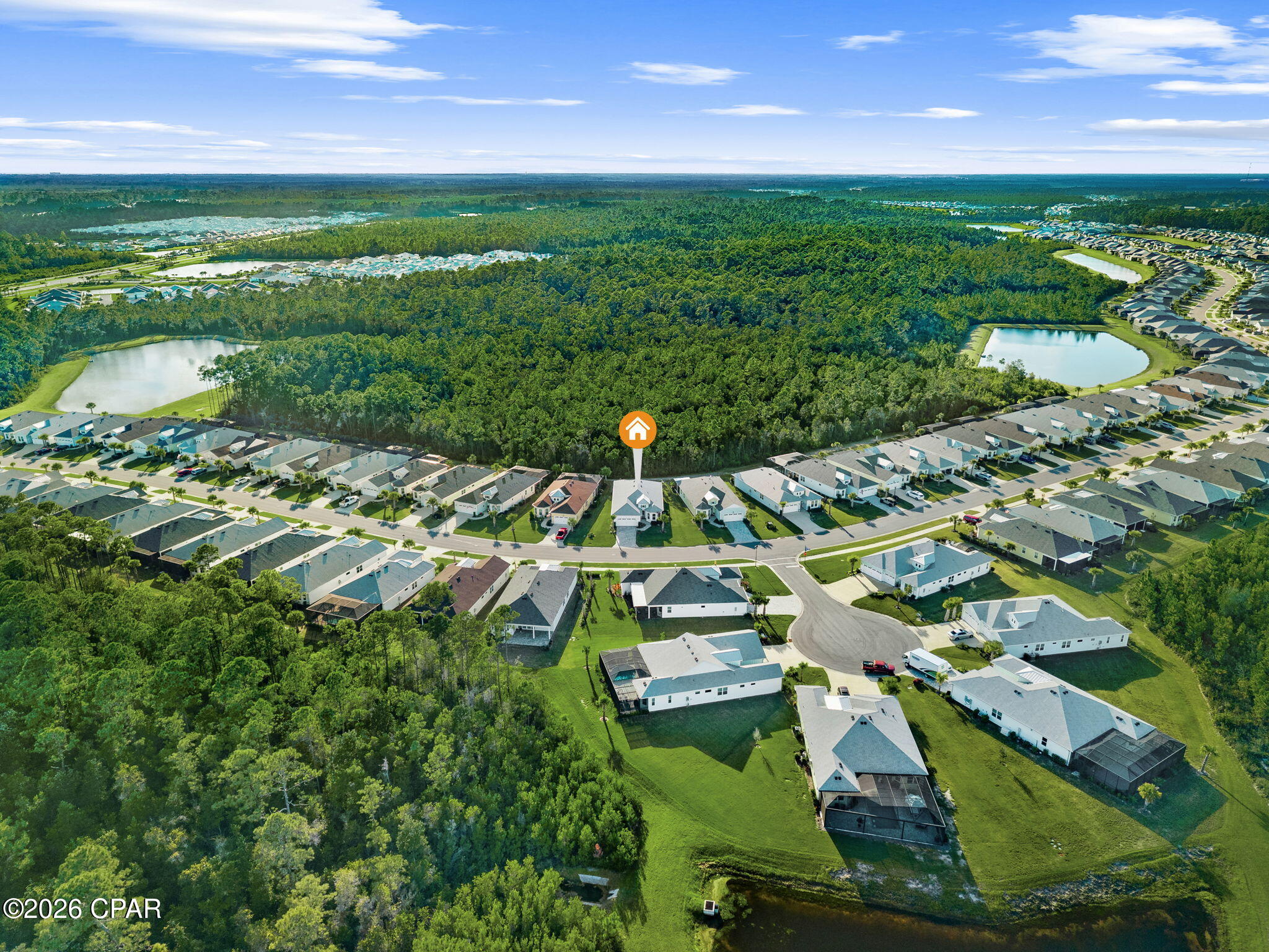 Aerial view of the marked home beside a wooded tract, surrounded by neighborhood streets and ponds.