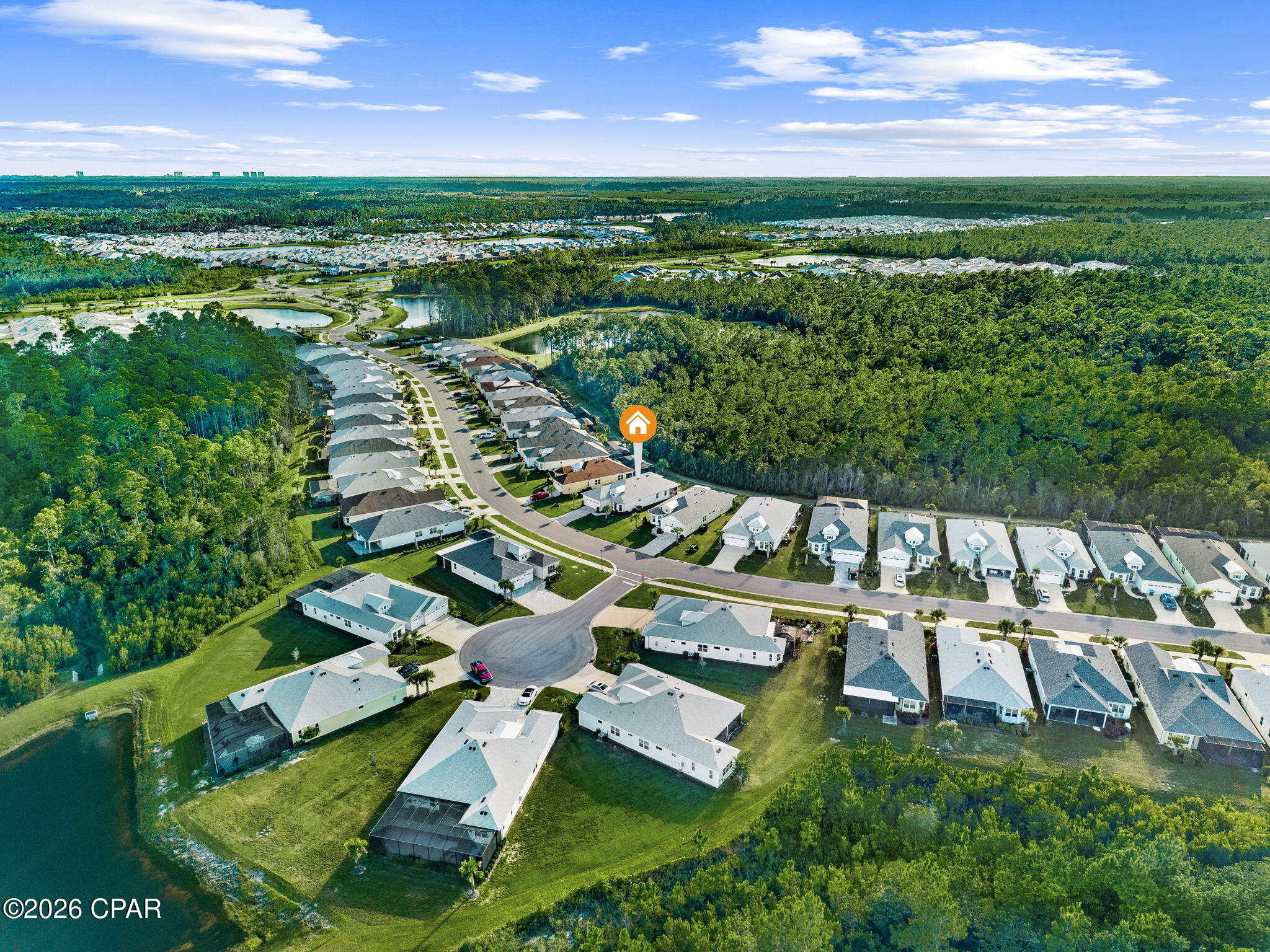 Aerial view of a marked home among neighborhood houses, ponds, and surrounding woodland.
