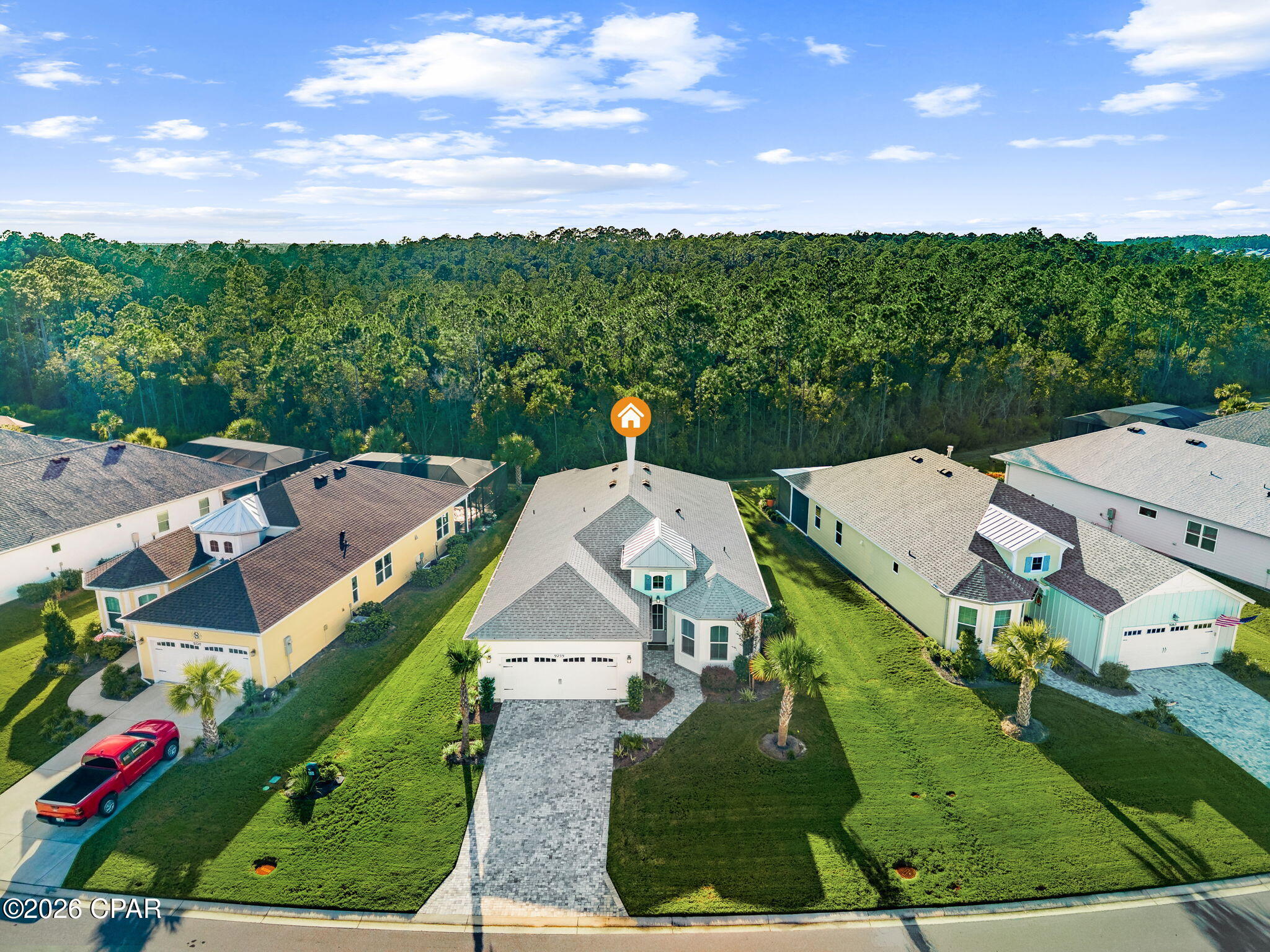 Aerial view of the home with a long paved driveway, neighboring houses, and woods behind the neighborhood.