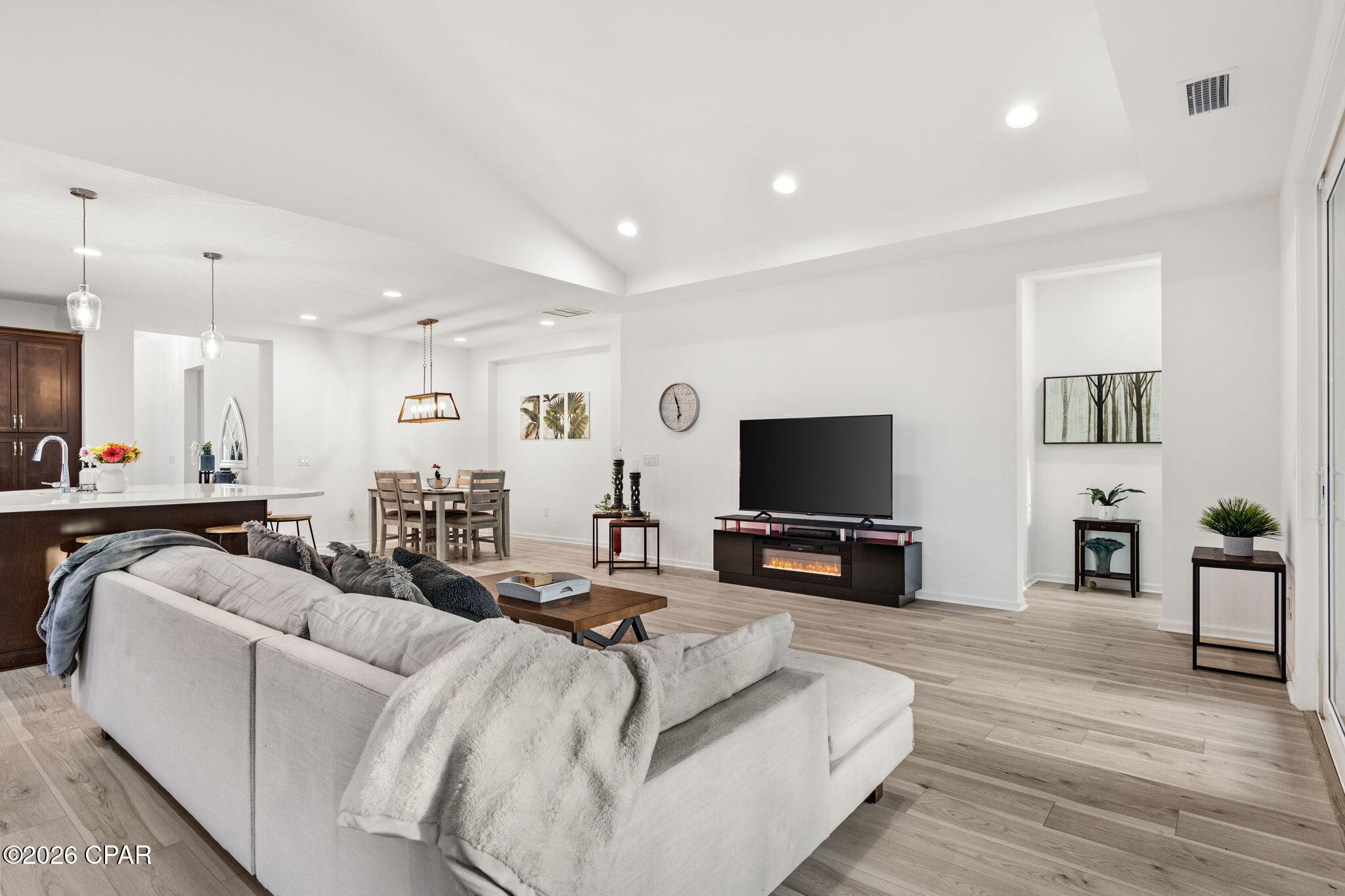 Open-plan living room with white sectional, television, electric fireplace, and dining area.