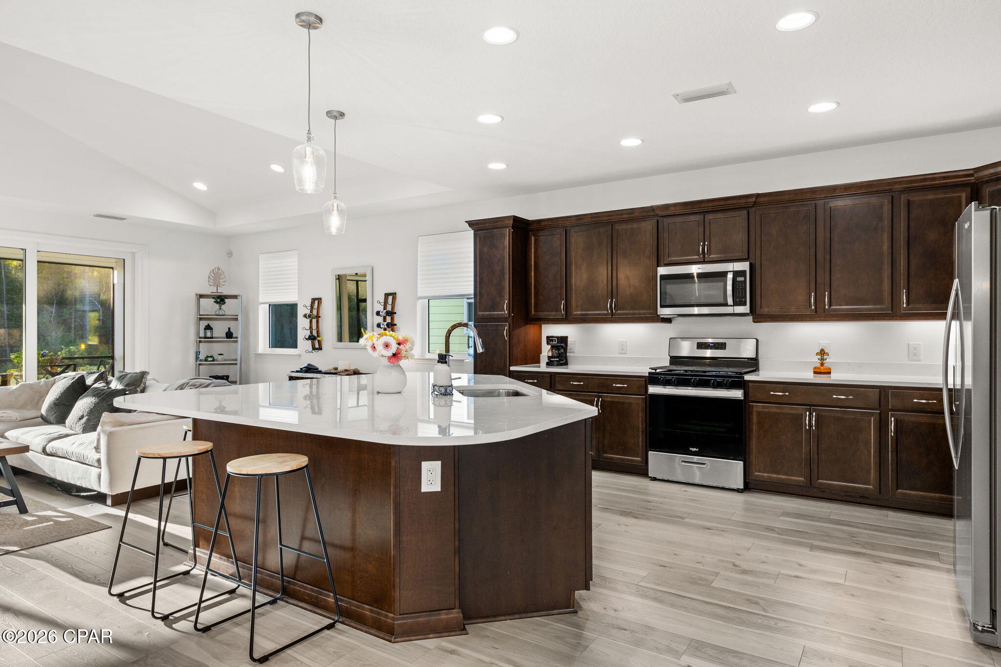Open-plan kitchen with a large white island, dark wood cabinets, stainless appliances, and nearby living area.