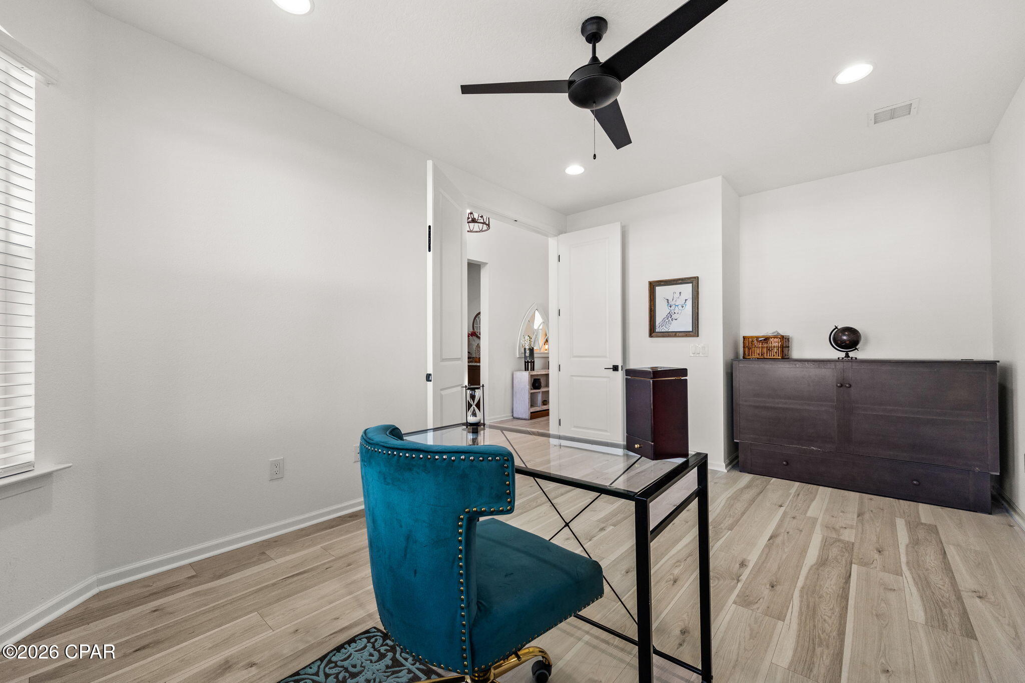 Furnished home office with a glass-top desk, teal chair, and dark sideboard.
