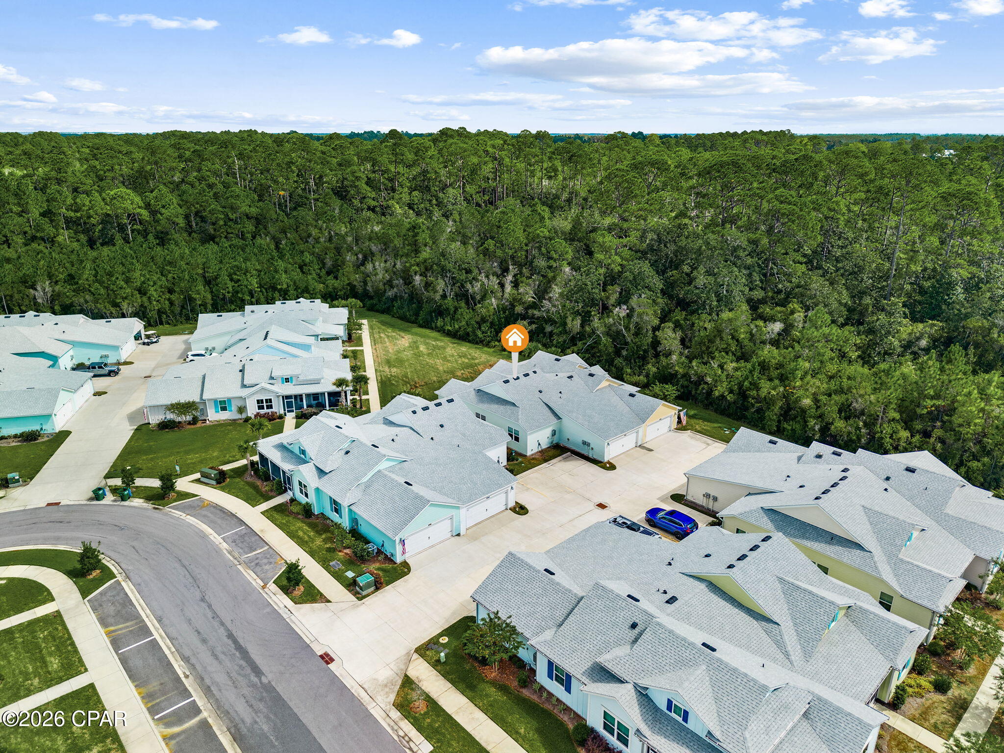 Aerial view of the marked home among light-roofed houses, beside a curved street and dense woodland.