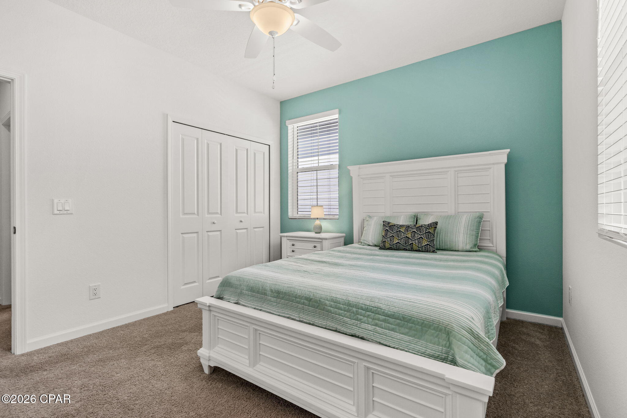 Bedroom with a white paneled bed and pale green bedding against a teal accent wall.