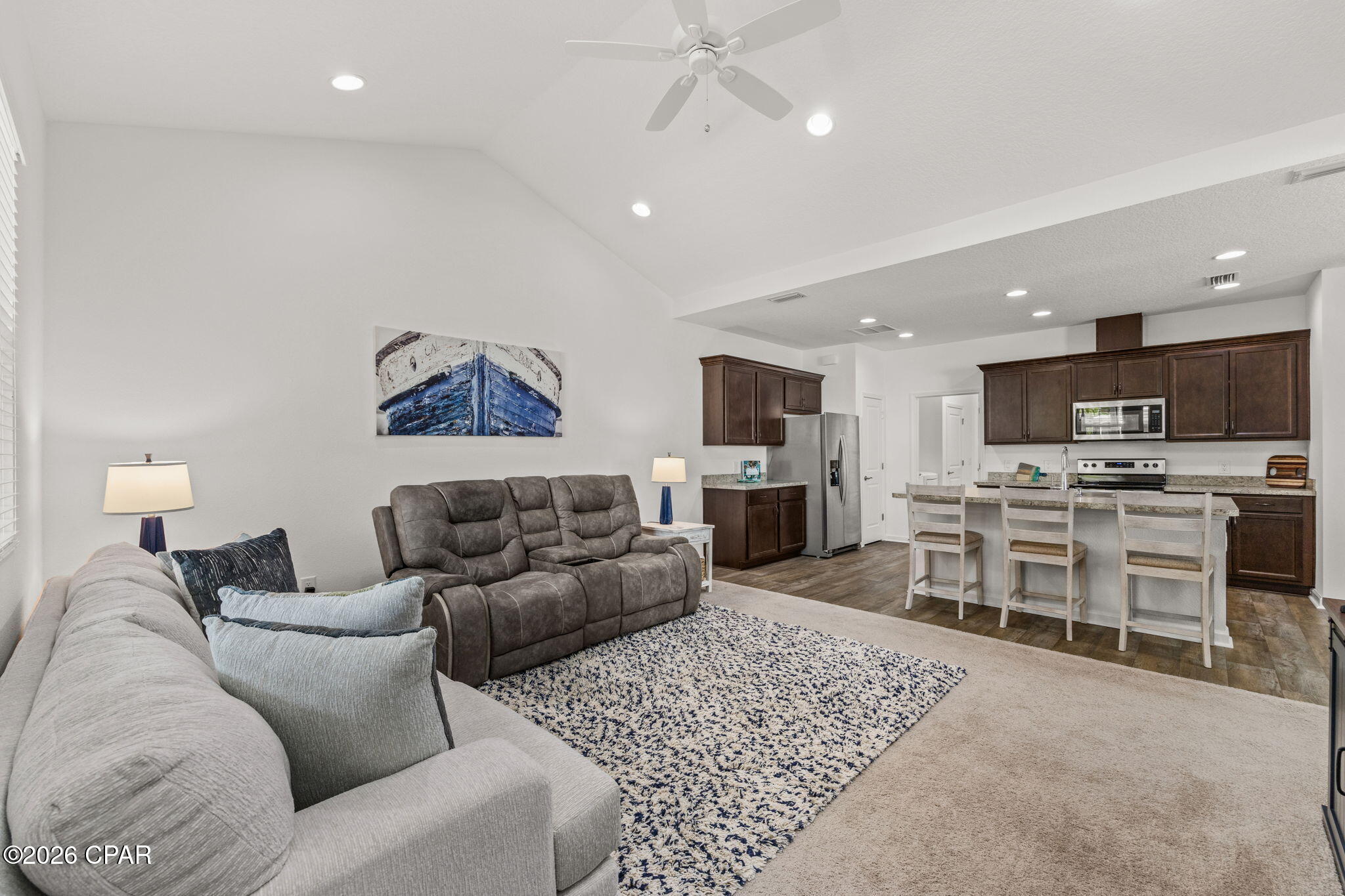 Living room opens to a kitchen with dark cabinetry, island seating, and ceiling fan.