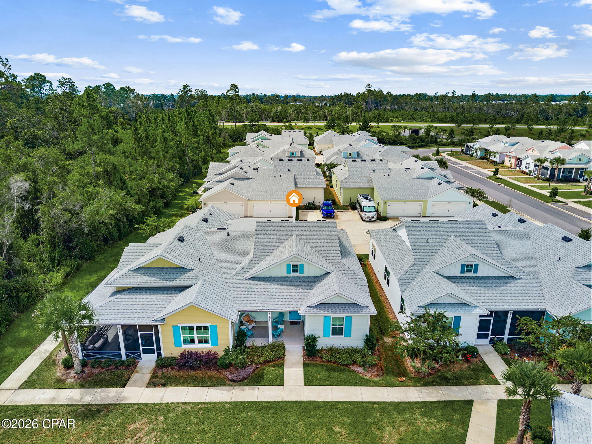 Aerial view of a neighborhood home marked with an orange house icon, beside wooded land.