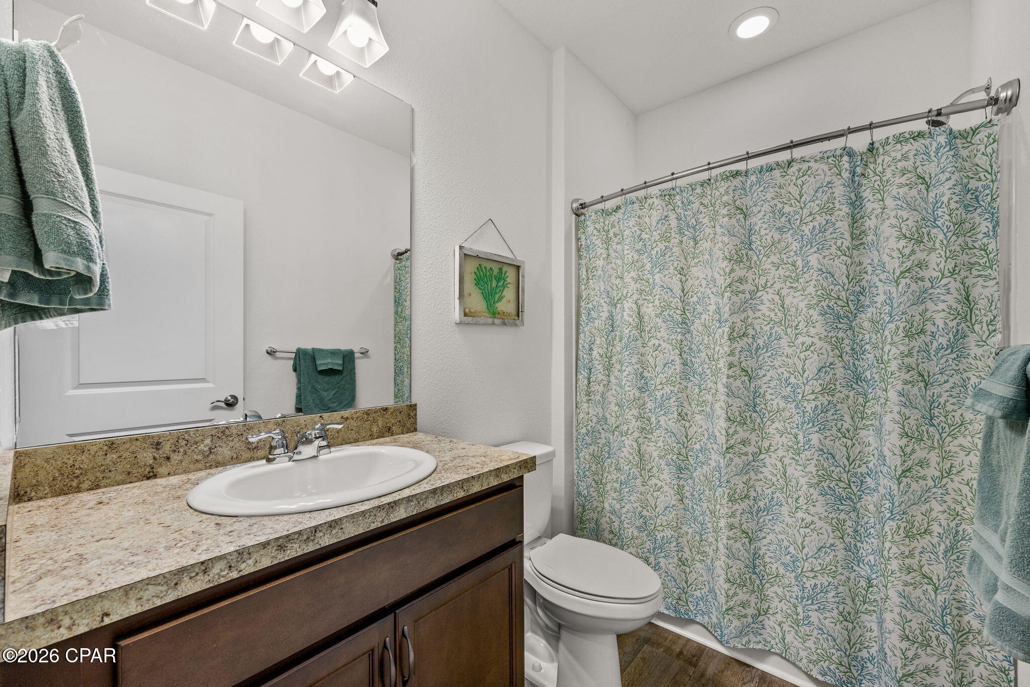 Bathroom with a dark wood vanity, speckled countertop, and green-and-blue patterned shower curtain.