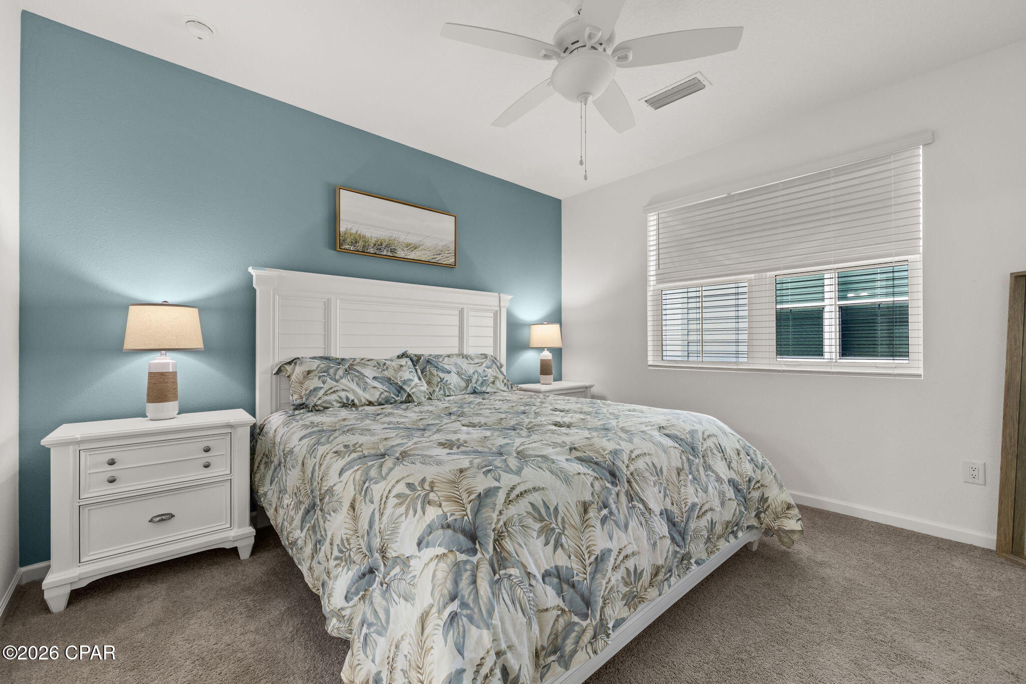 Bedroom with botanical-print bedding, white furniture, and a teal accent wall.