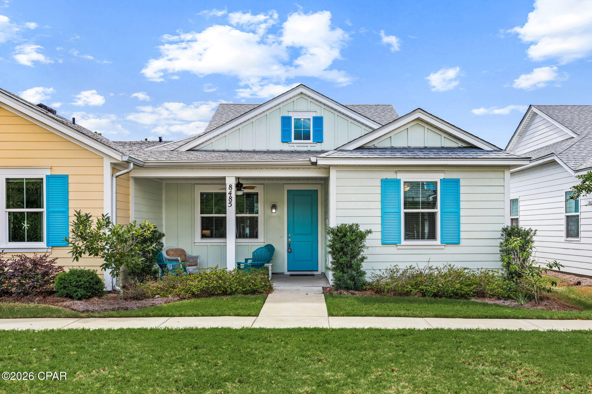 House exterior with a covered porch, turquoise door and shutters, and landscaped front lawn.
