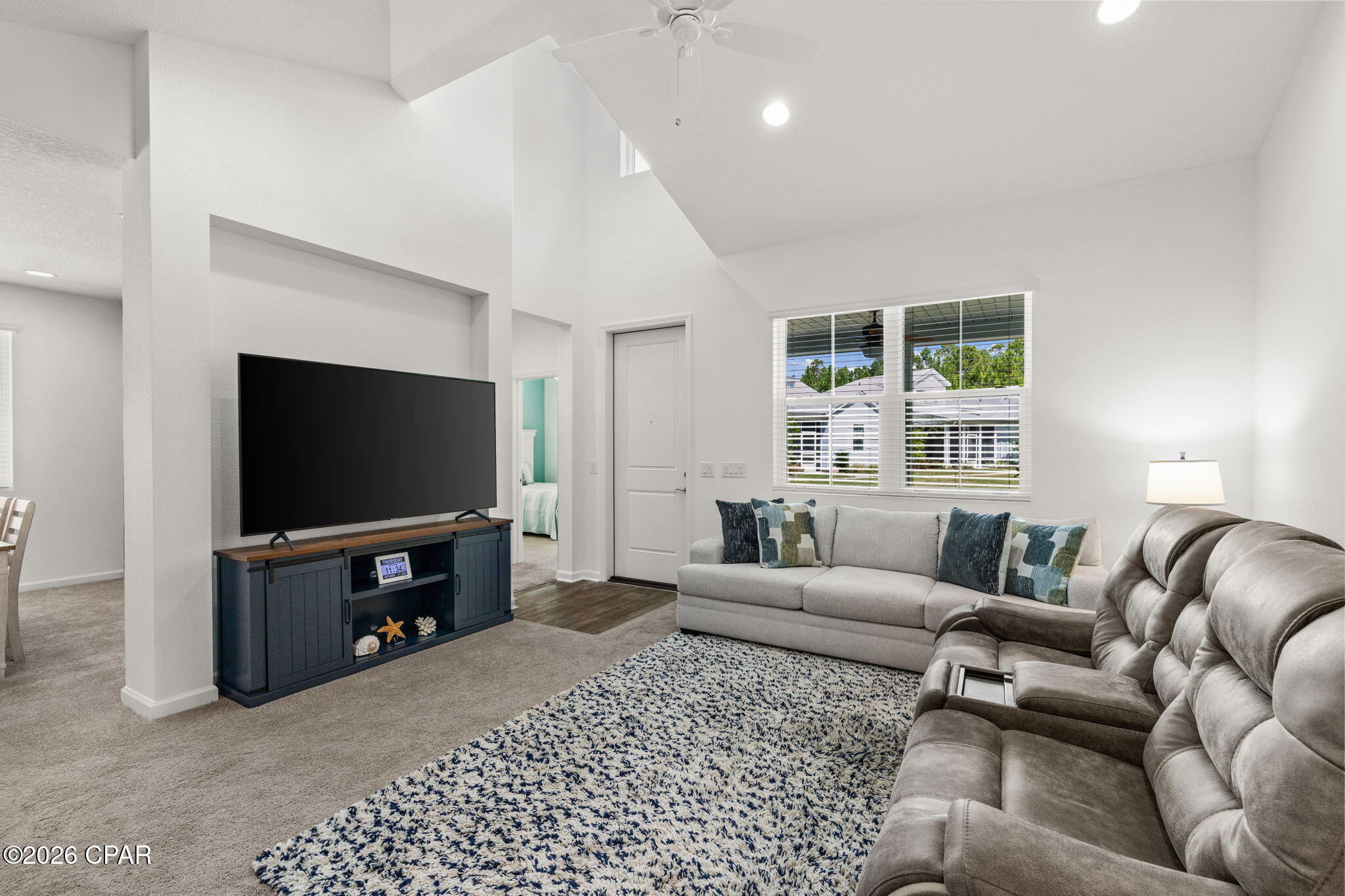 Living room with a vaulted ceiling, gray sectional sofas, a large television, and a blue-and-white rug.