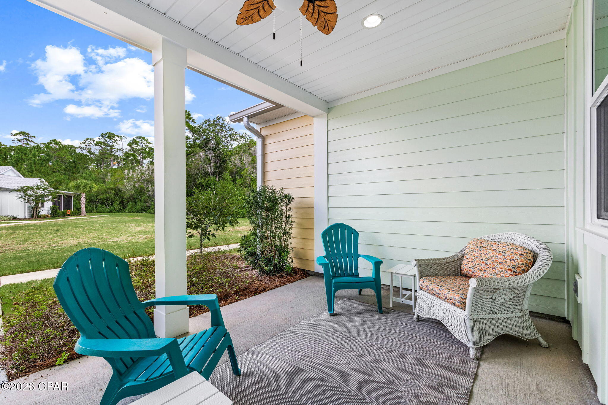 Covered porch with teal Adirondack chairs and white wicker seating overlooking a green lawn.