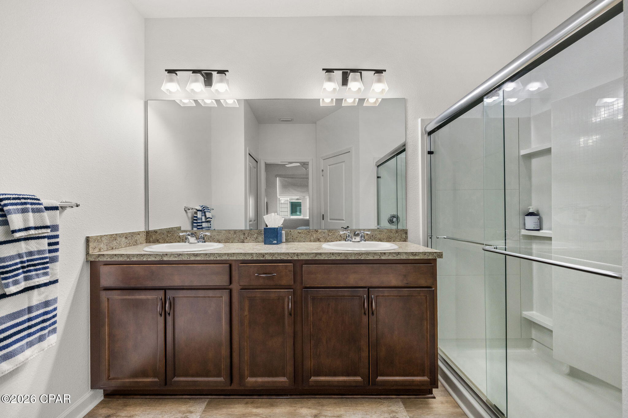 Bathroom with a dark wood double vanity and glass-enclosed shower with built-in shelves.