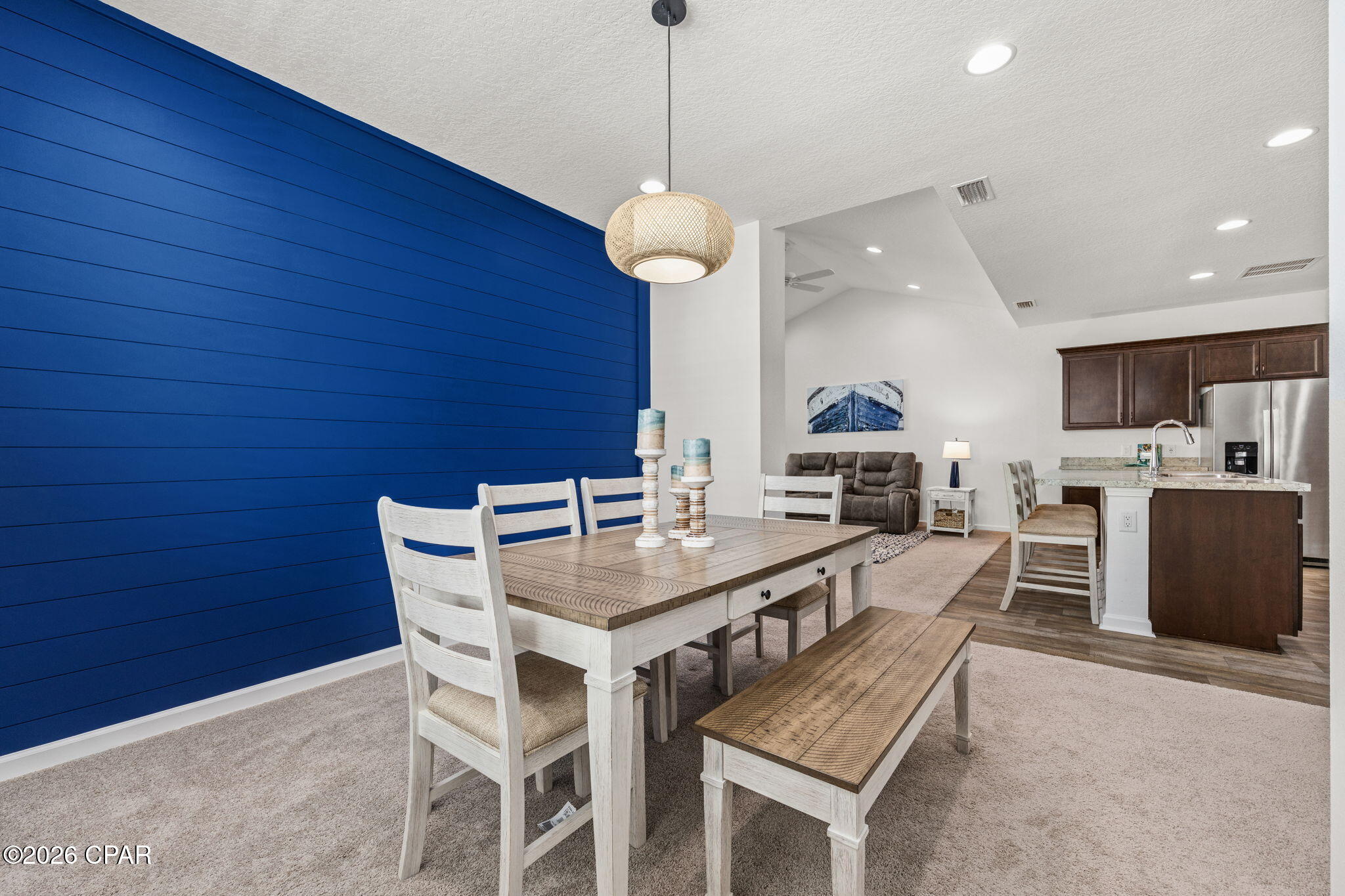 Dining area with a white table and bench beside a navy-blue accent wall, opening to the kitchen and living room.