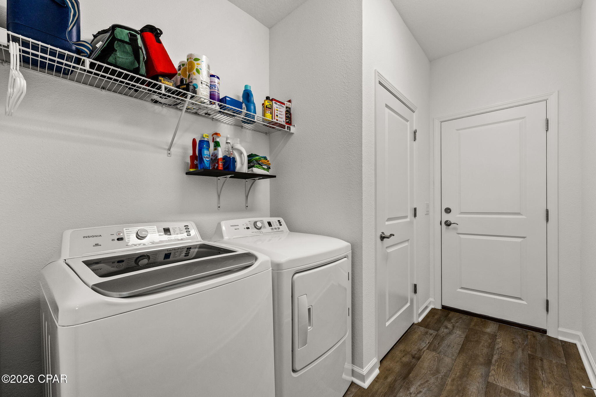 Laundry room with washer and dryer, storage shelves, and dark wood-look flooring.