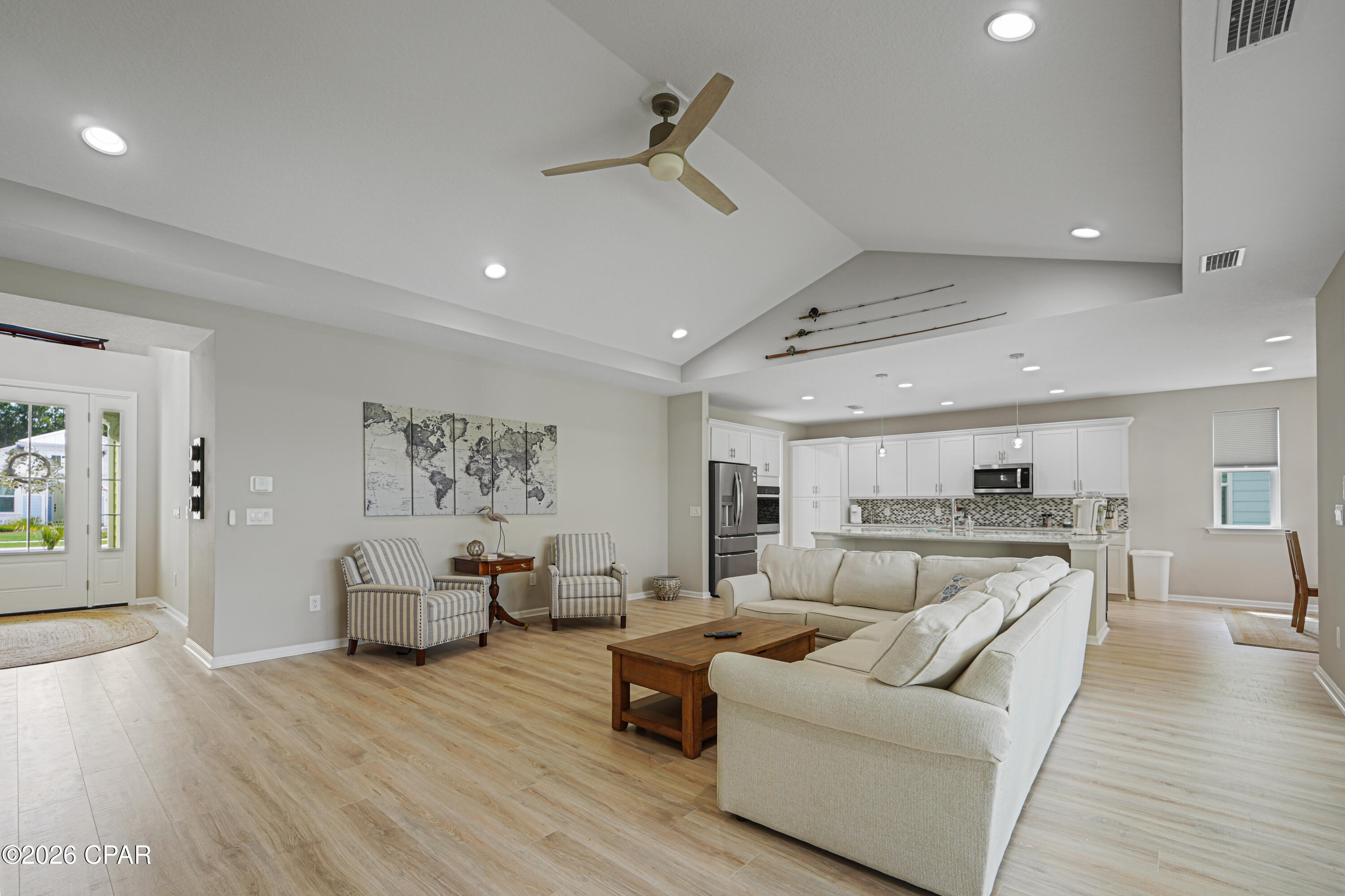 Open-concept living room with a white sectional, striped chairs, vaulted ceiling, and kitchen beyond.