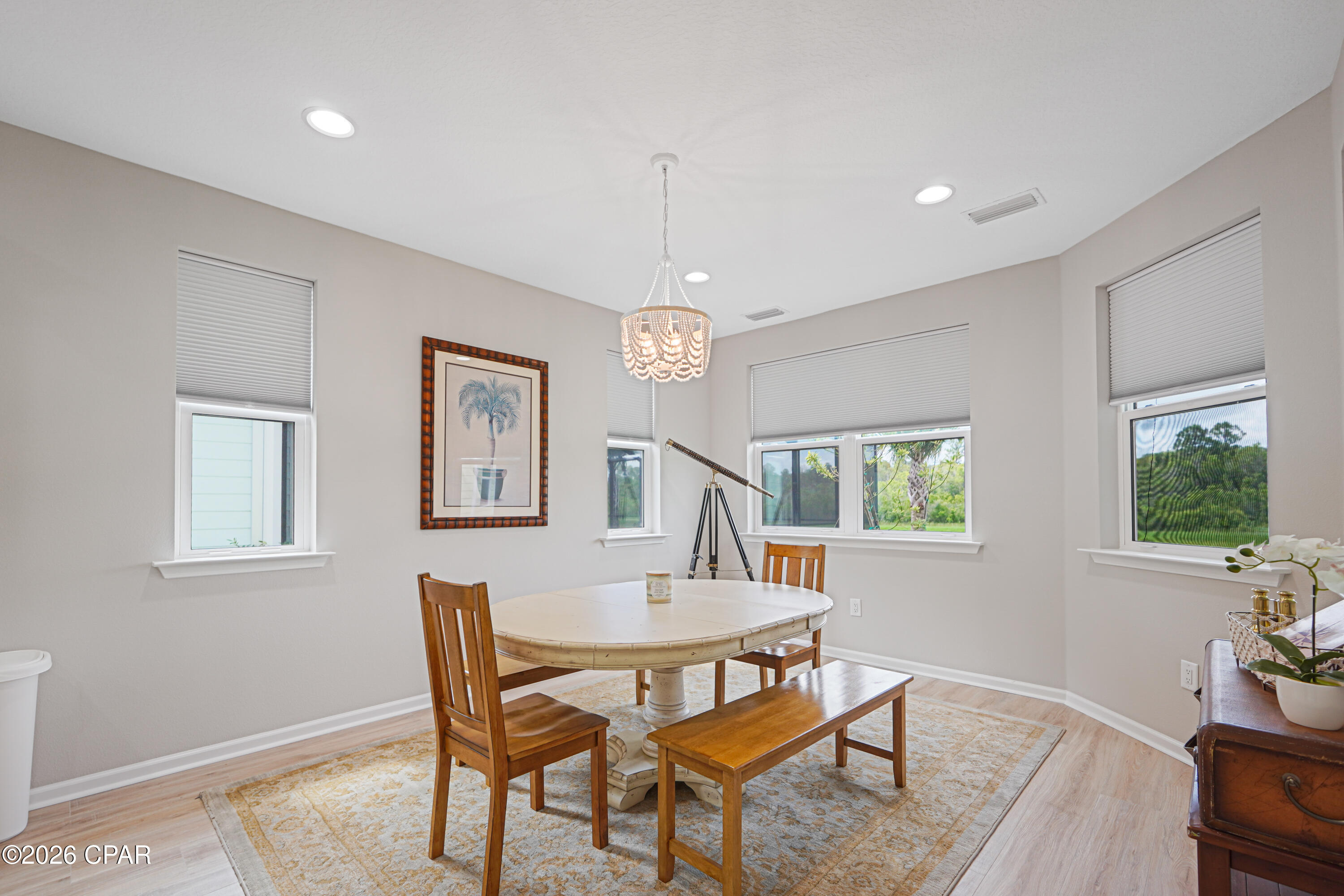 Dining room with a round table, wooden chairs, a telescope, and windows overlooking greenery.