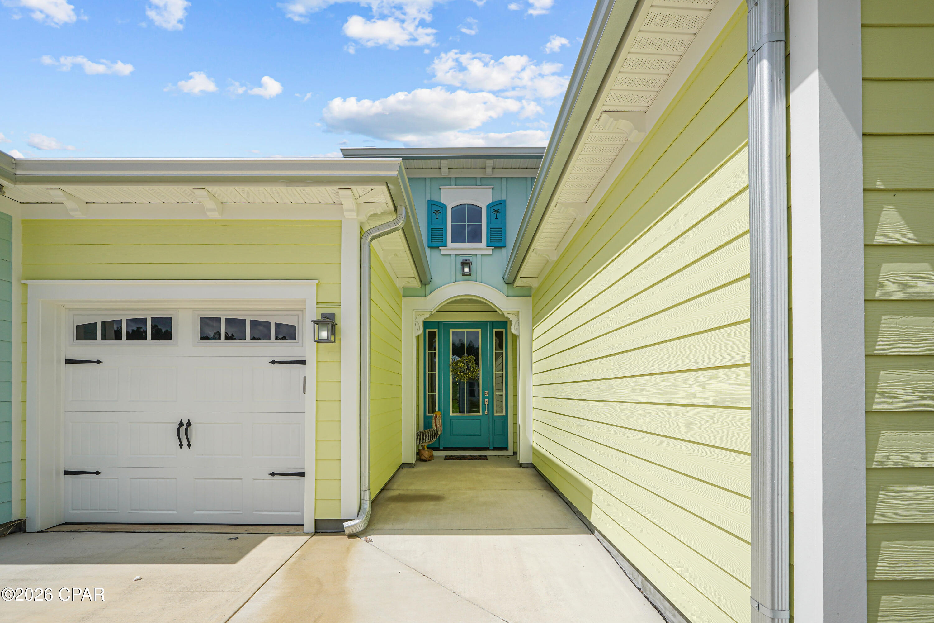 Pastel yellow home exterior with a teal front door, arched entry, blue shutters, and white garage door.