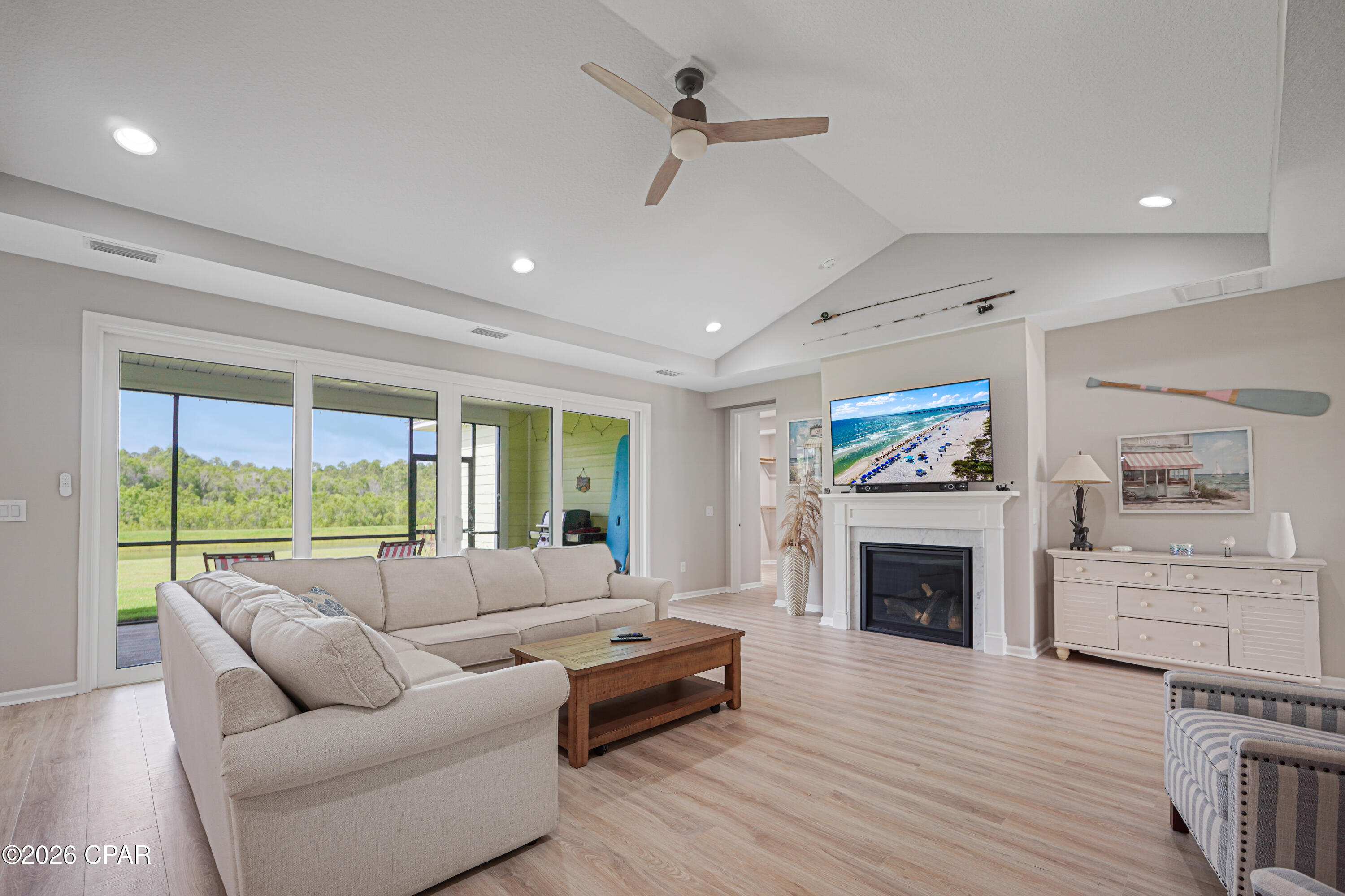 Living room with a vaulted ceiling, large sectional, fireplace, and sliding doors overlooking a grassy yard.