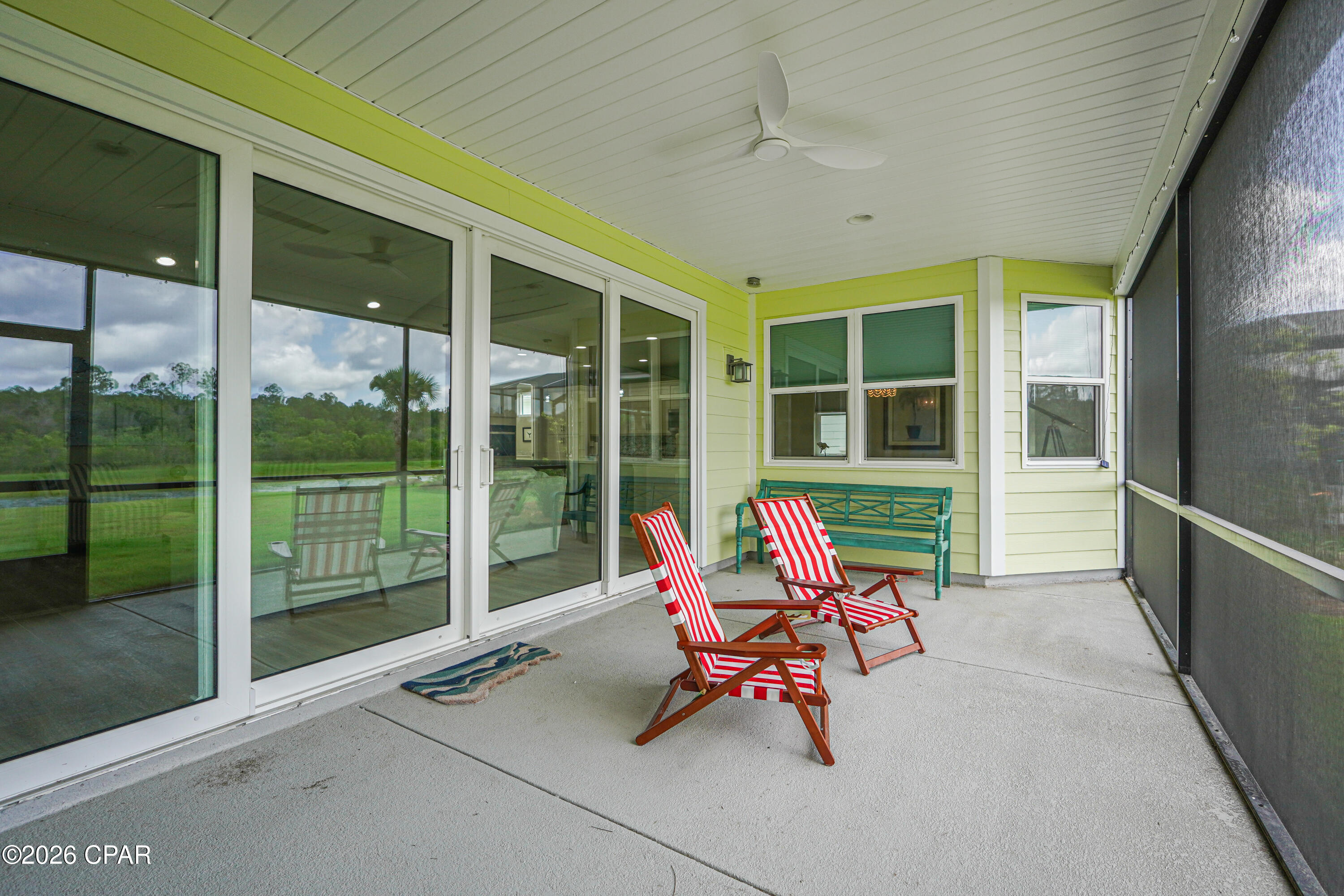 Covered patio with striped chairs and a teal bench beside sliding glass doors.