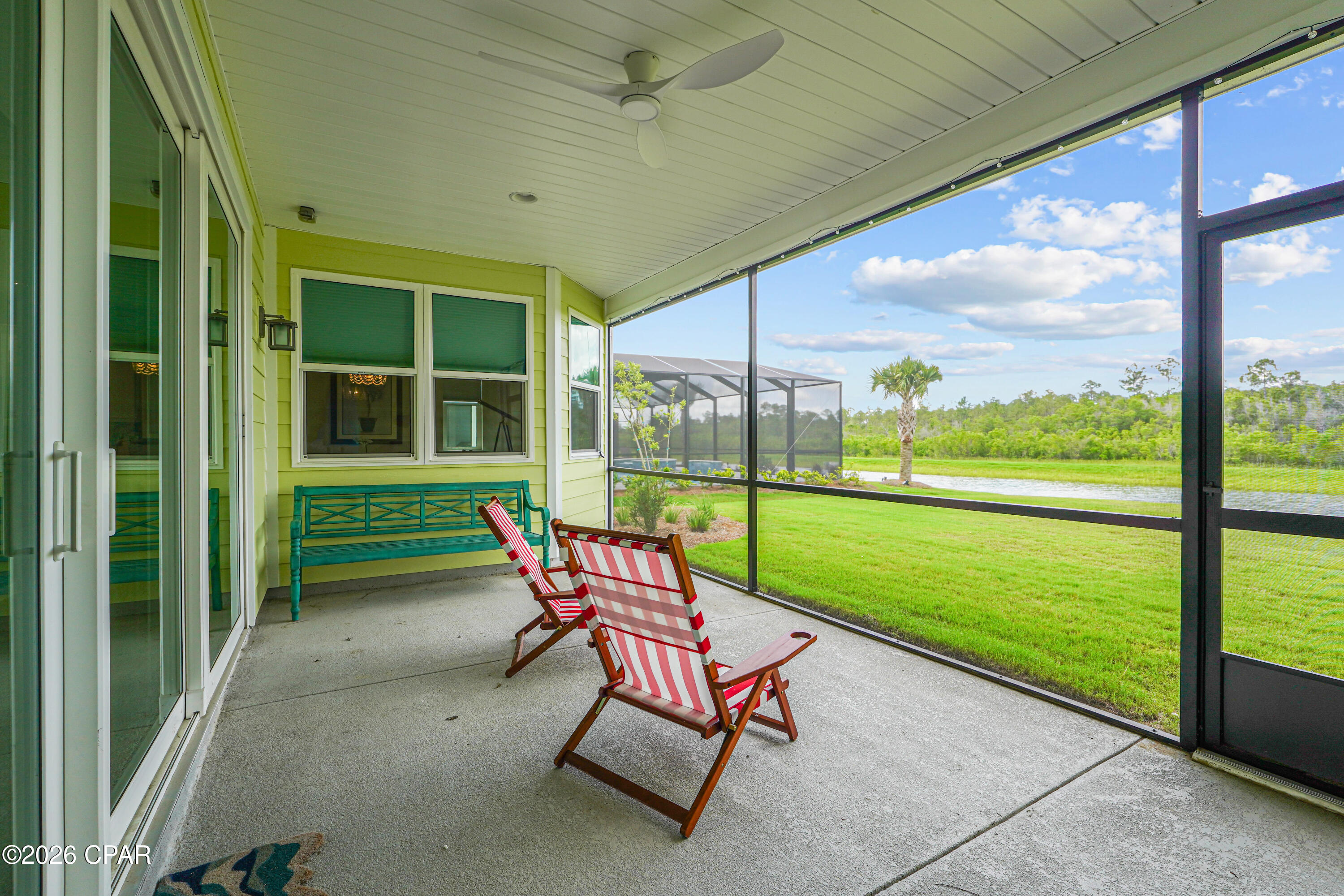 Screened porch with striped chairs and a turquoise bench overlooking a lawn and pond.