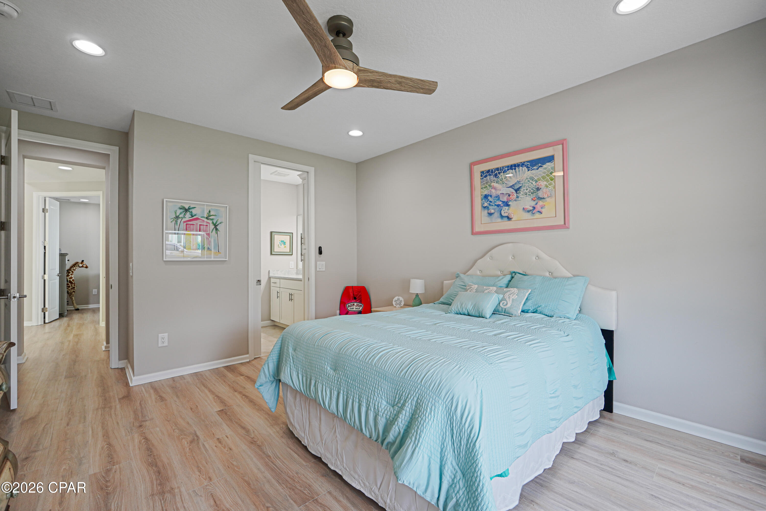 Furnished bedroom with a large bed in light blue bedding and a wood-blade ceiling fan.