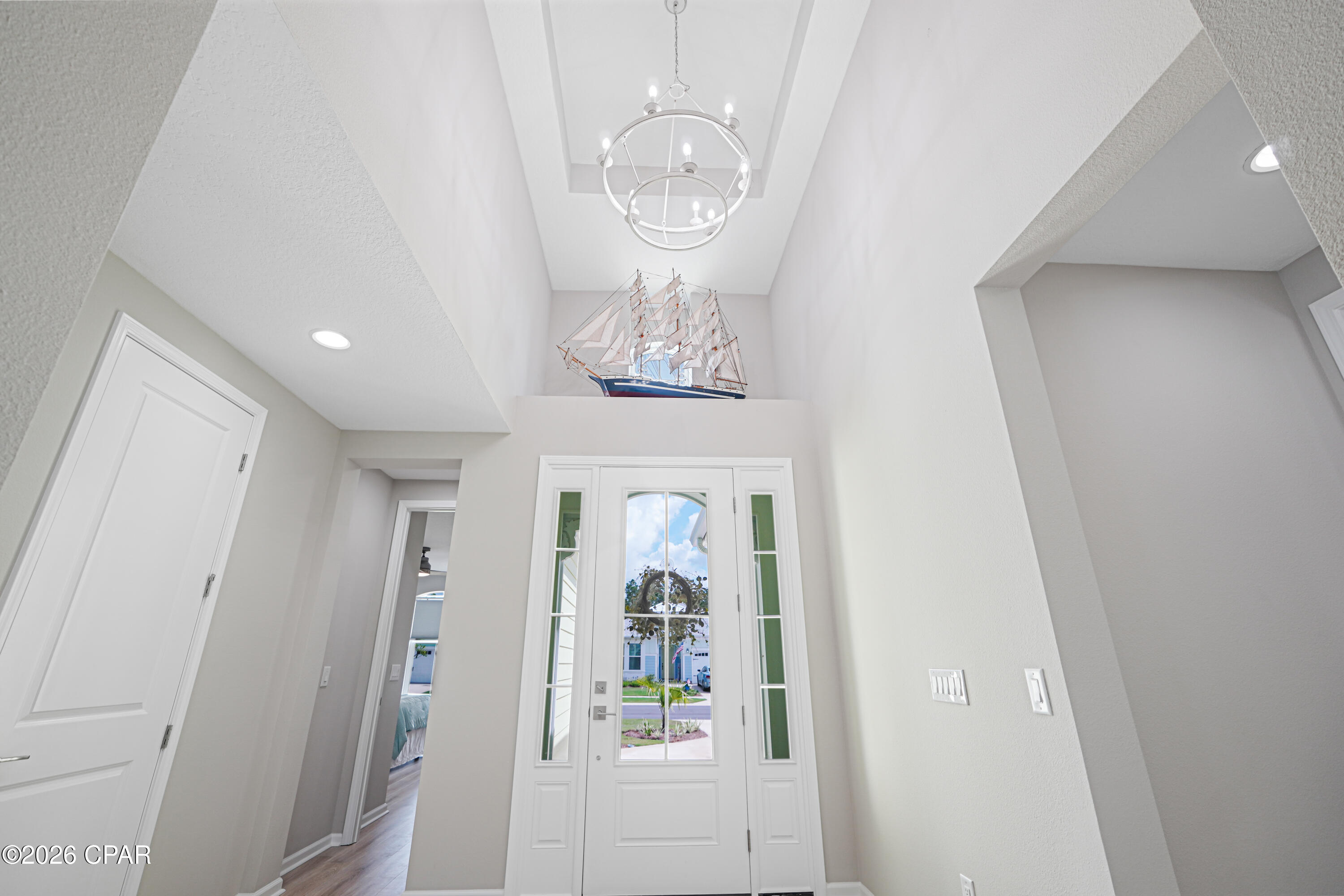 Entry foyer with a tall ceiling, circular chandelier, model sailing ship, and glass-paneled front door.
