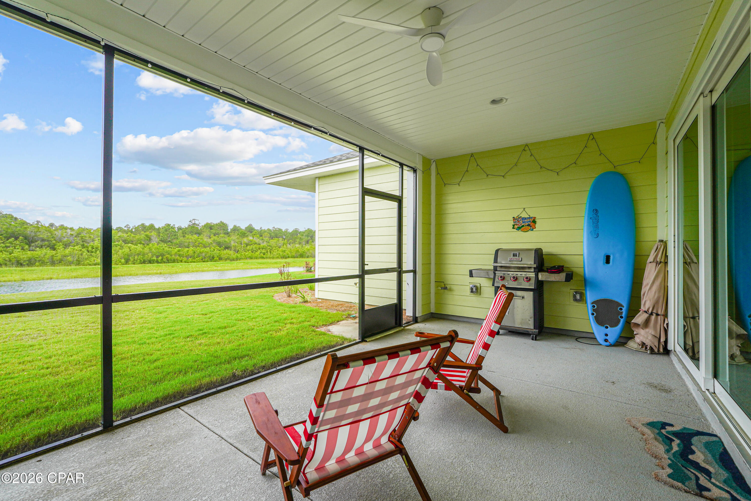 Screened porch with striped lounge chairs and grill overlooking a pond.