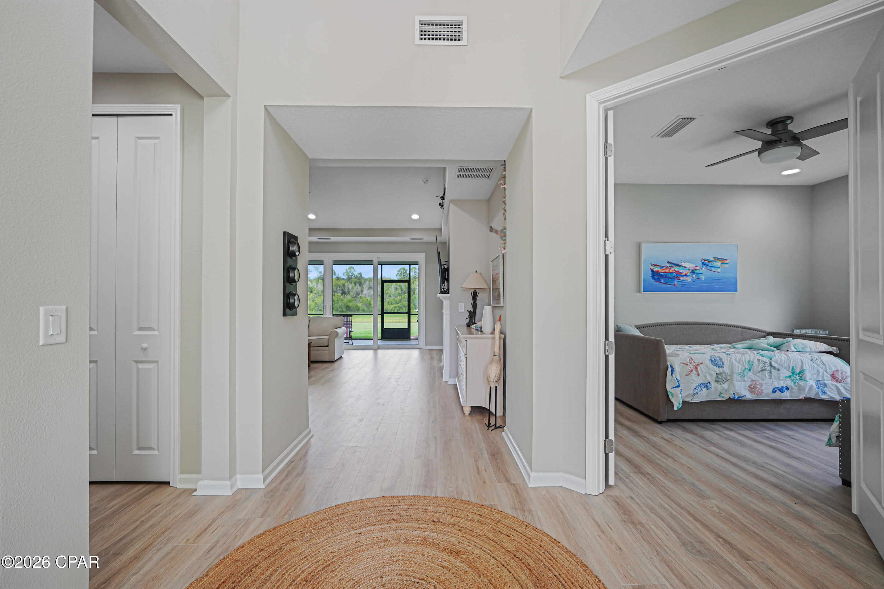 Bright hallway opens toward the living area, with a furnished coastal-style bedroom on the right.