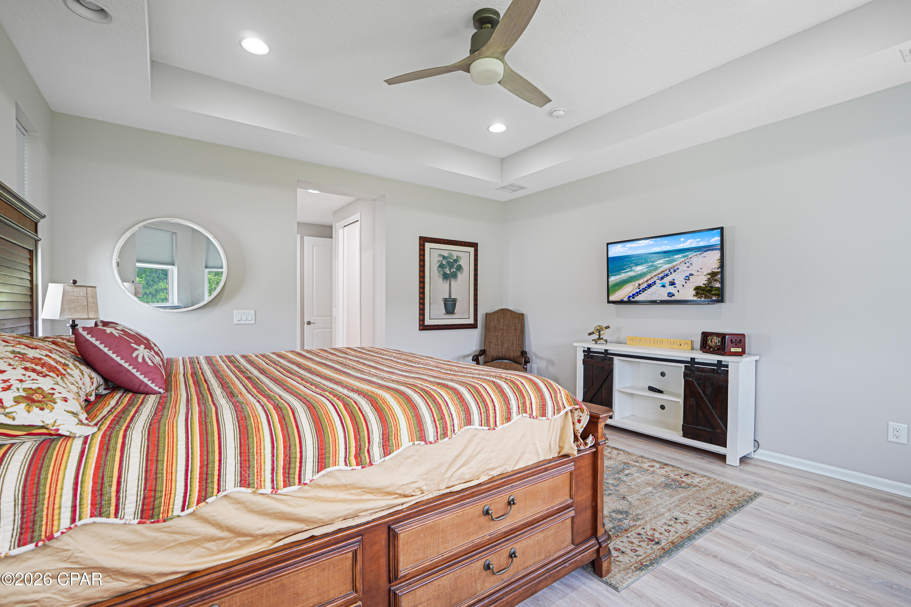 Furnished bedroom with a wooden bed, colorful striped quilt, ceiling fan, and television.