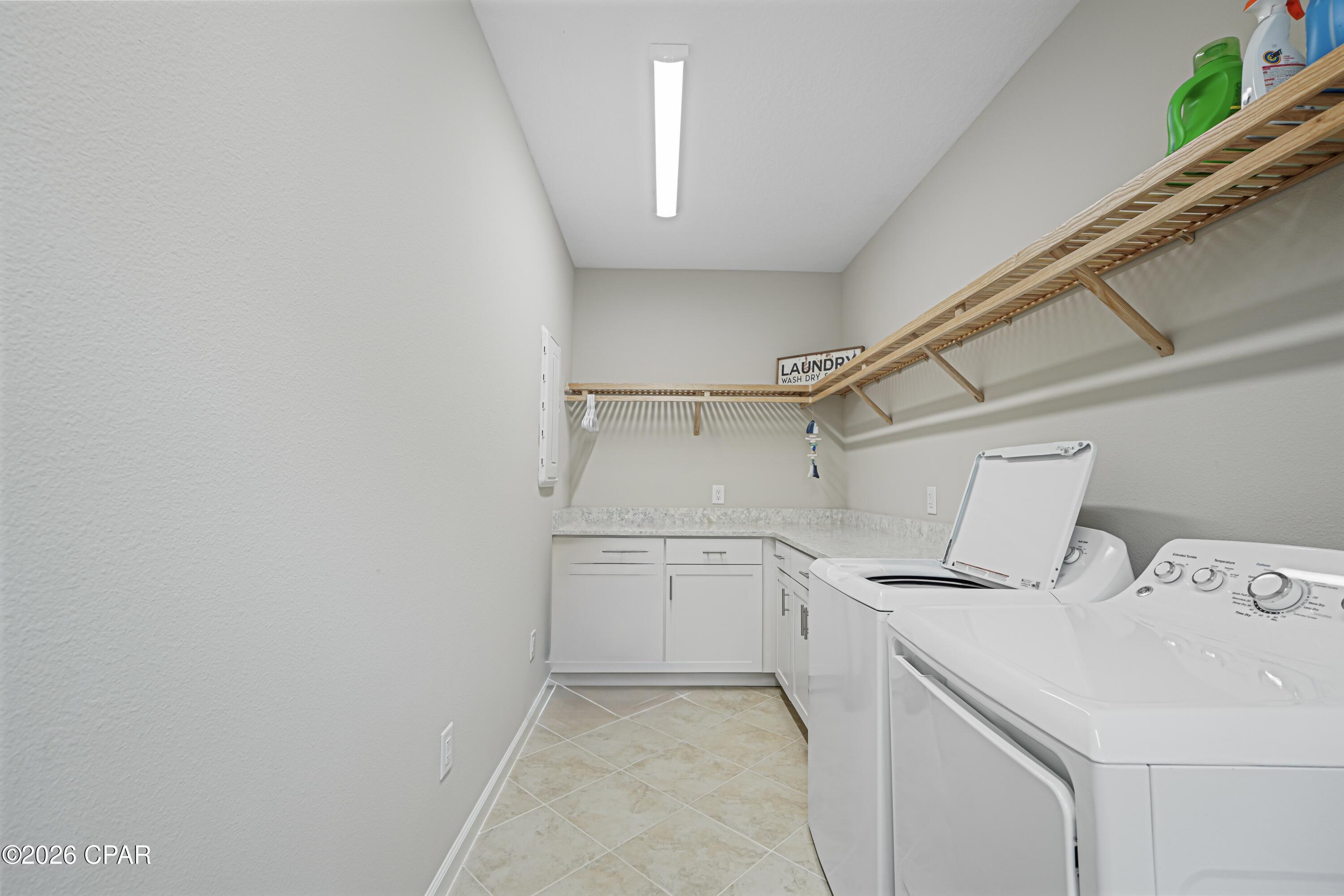 Laundry room with washer and dryer, wraparound cabinets, and open wooden shelves.