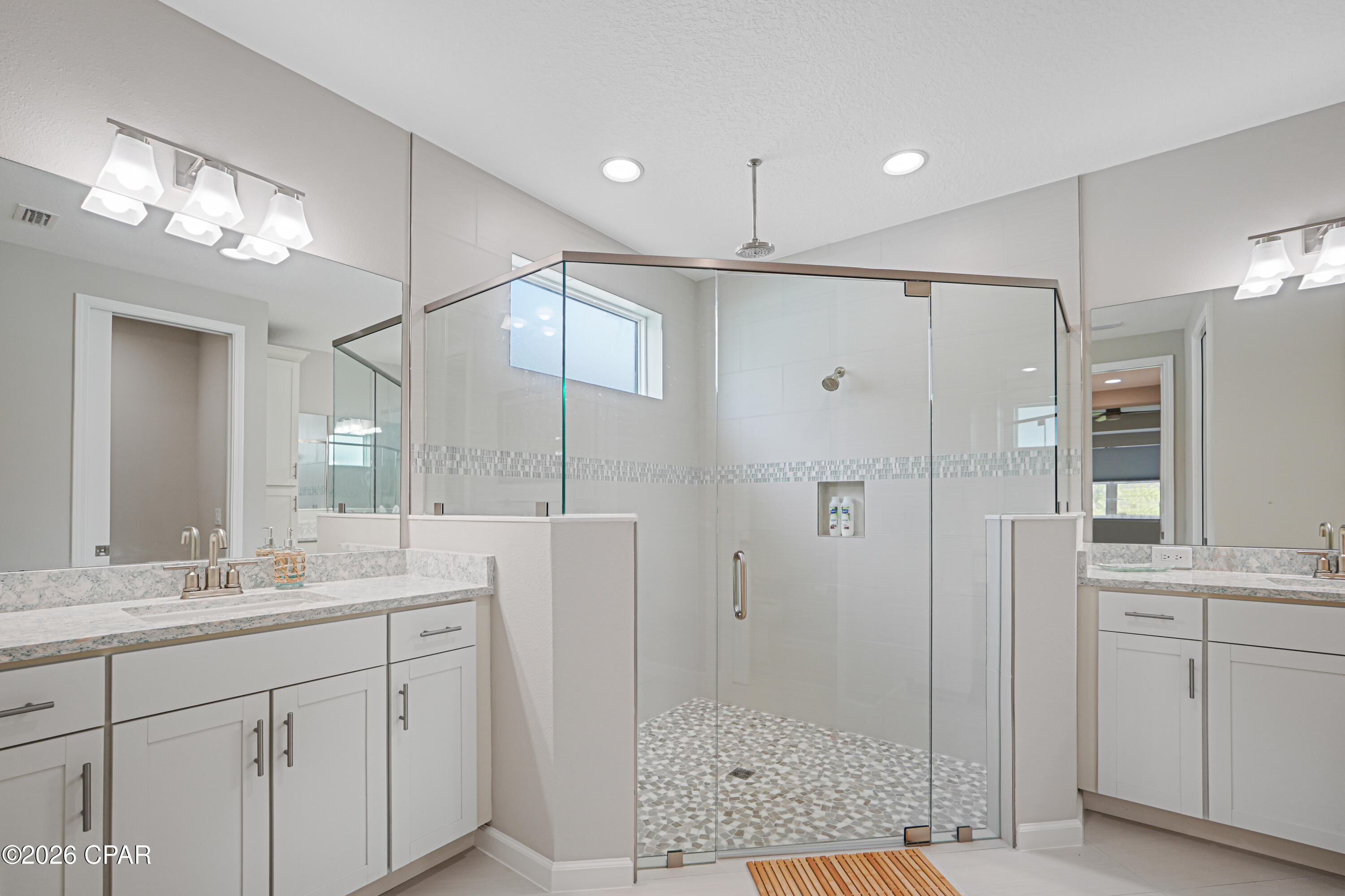 Primary bathroom with a spacious glass shower, mosaic tile floor, and white double vanities.